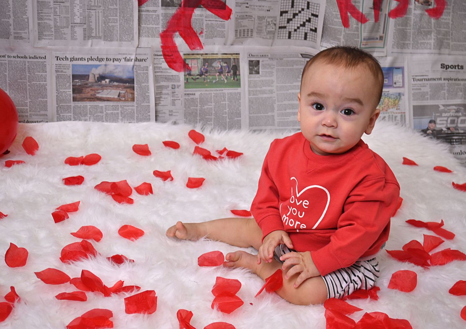 Baby in a red Valentine's outfit sitting among rose petals during a studio session by an Orlando Florida Photographer.
