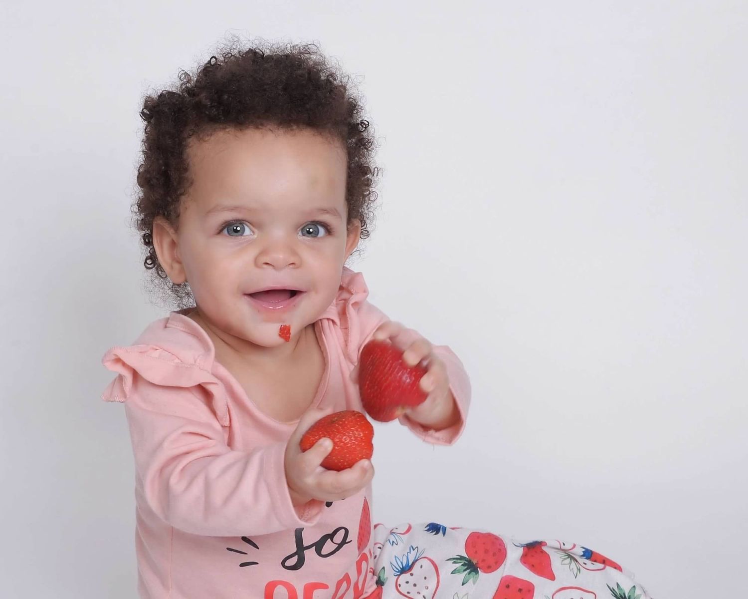 Smiling baby holding a strawberry during a milestone session by a Central Florida Photographer.