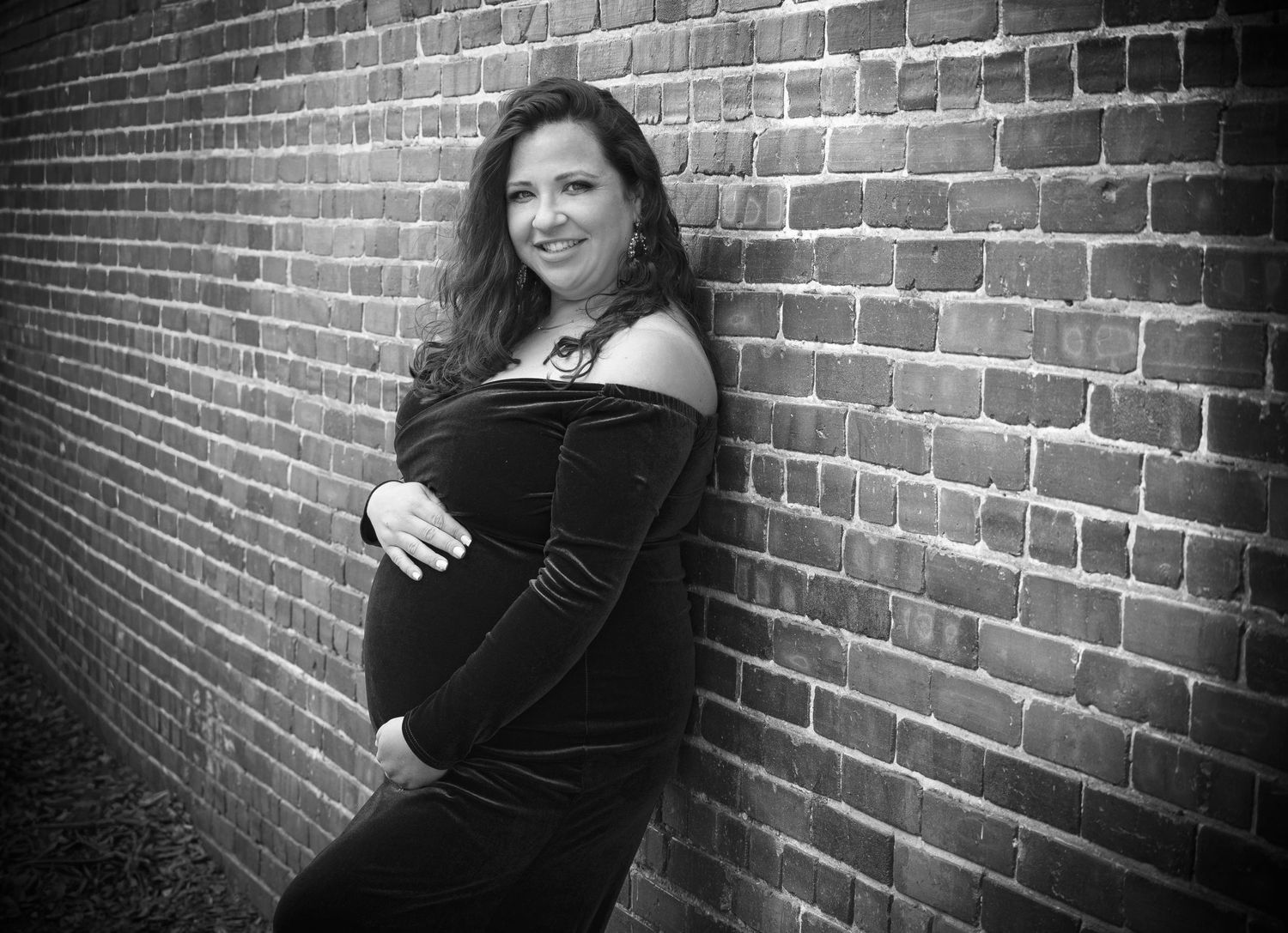 Black and white maternity portrait of an expectant mother beside a brick wall by a Central Florida Photographer.