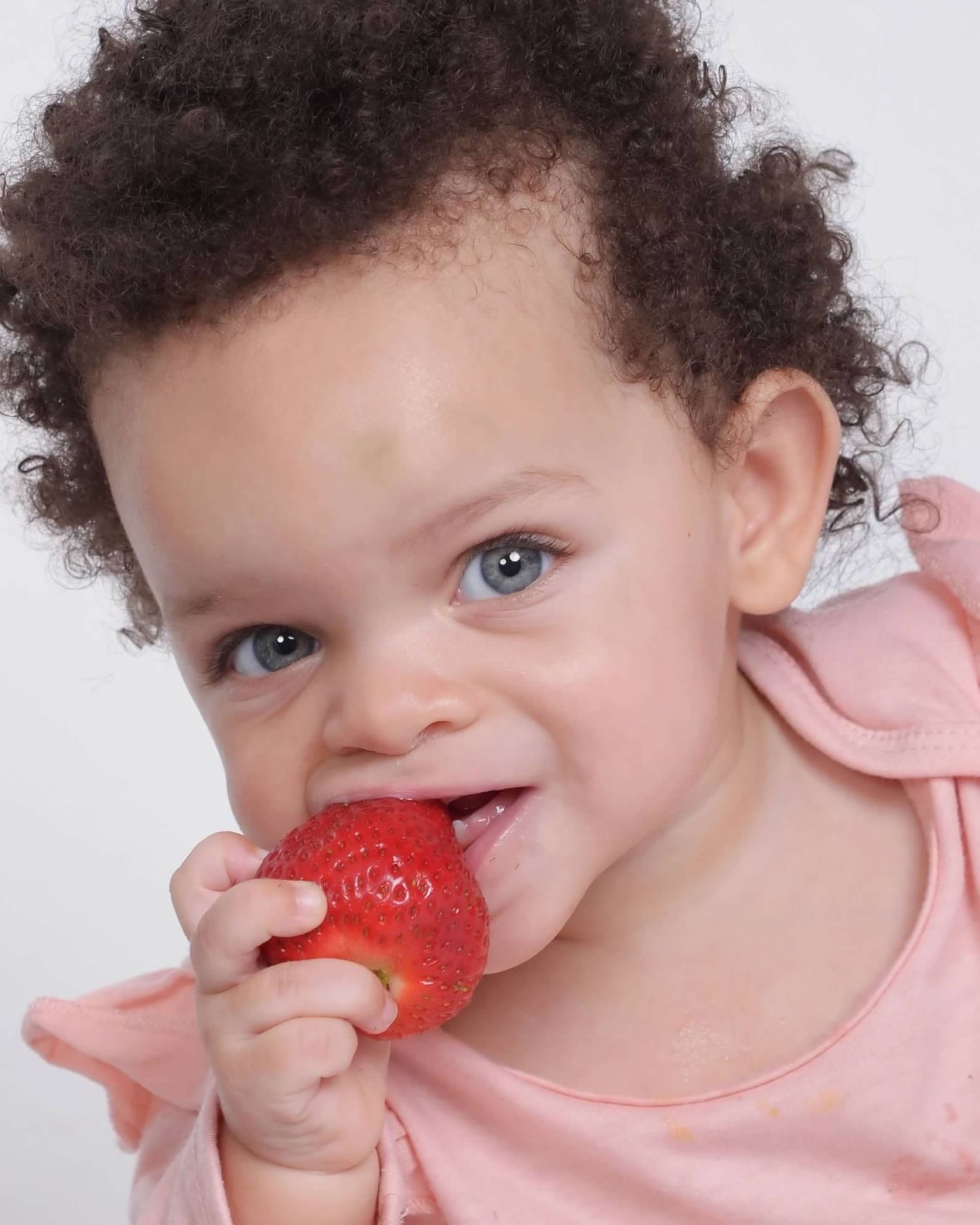 Close-up of a baby holding a strawberry during a Milestone portrait by a Central Florida Photographer.