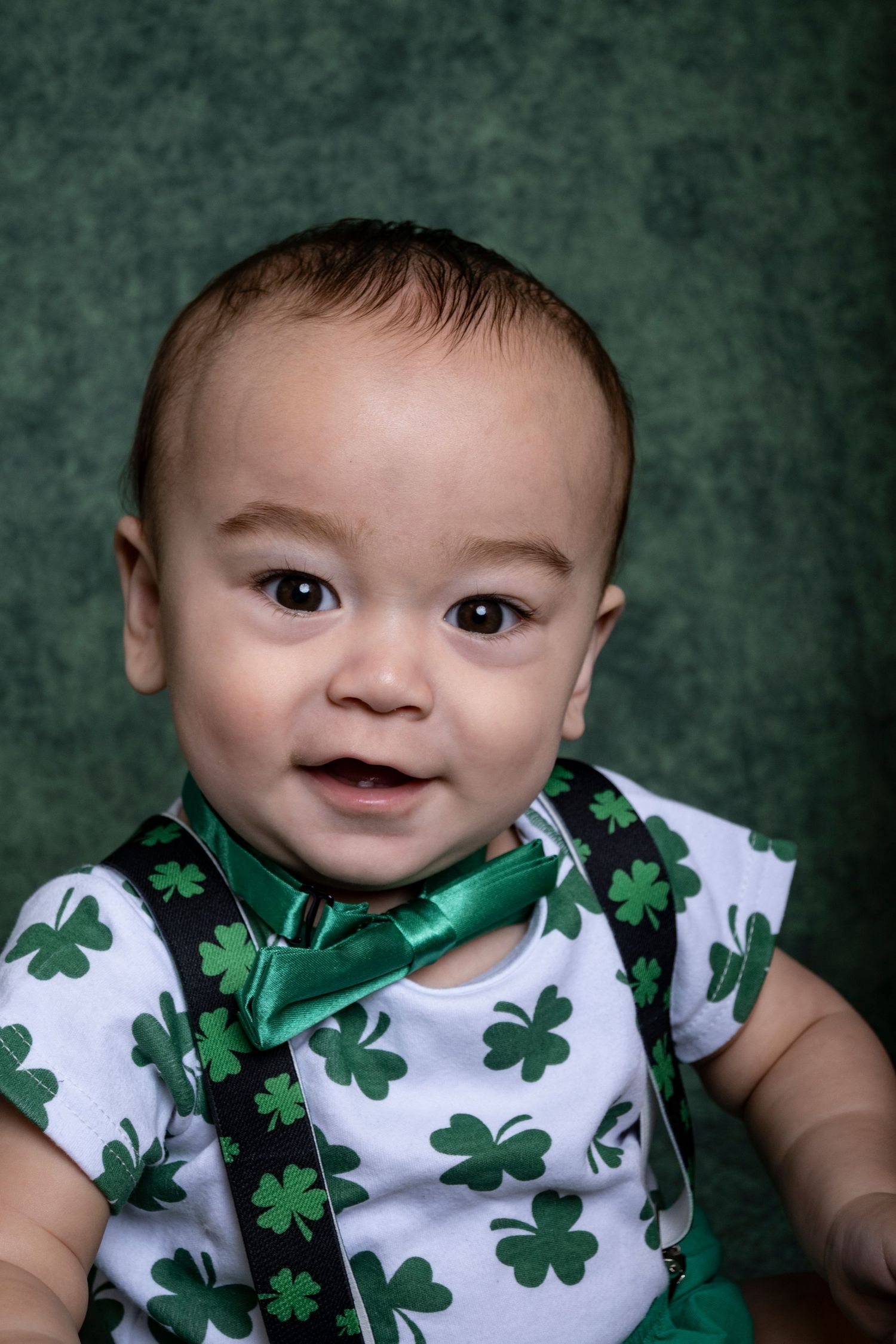 Baby in shamrock overalls smiling during a holiday milestone session by a Central Florida Photographer.
