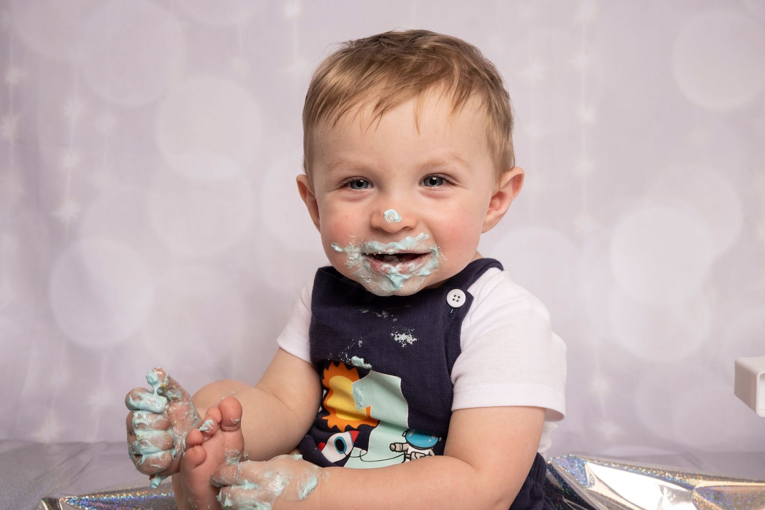 Close-up of a toddler with blue frosting on his face during a first birthday cake smash by Teagan Rae Lens