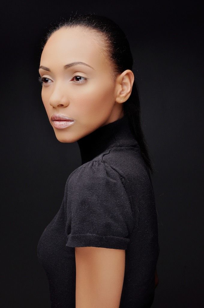 A young woman in a black turtleneck top poses against a dark background with sleek hair pulled back.