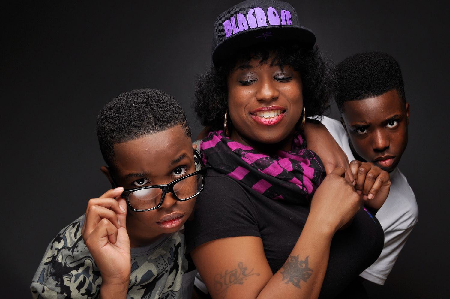 Three people pose together in a studio portrait, with a woman in a hat and scarf flanked by two young men.