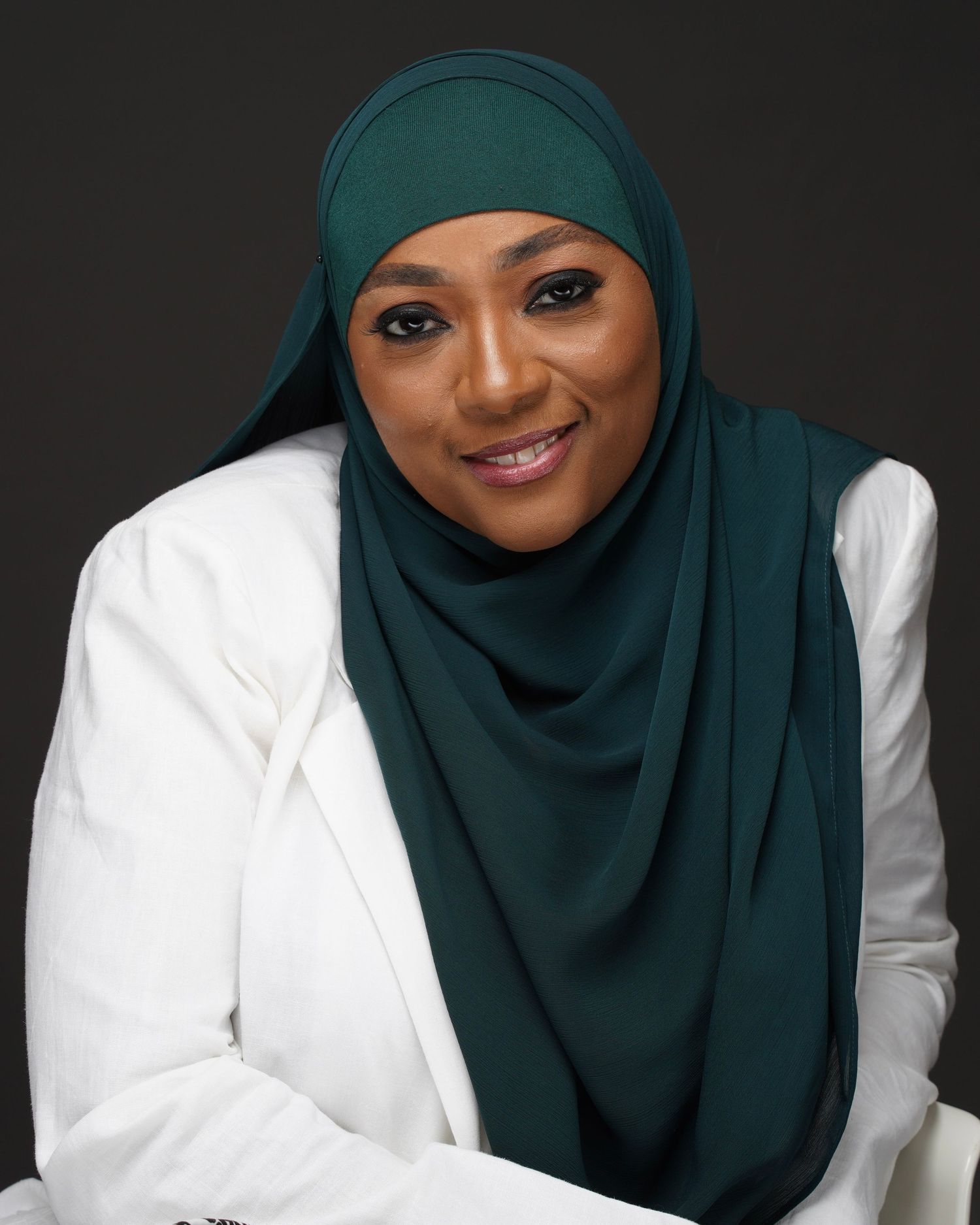 Woman wearing teal hijab and white blazer smiling in professional portrait.