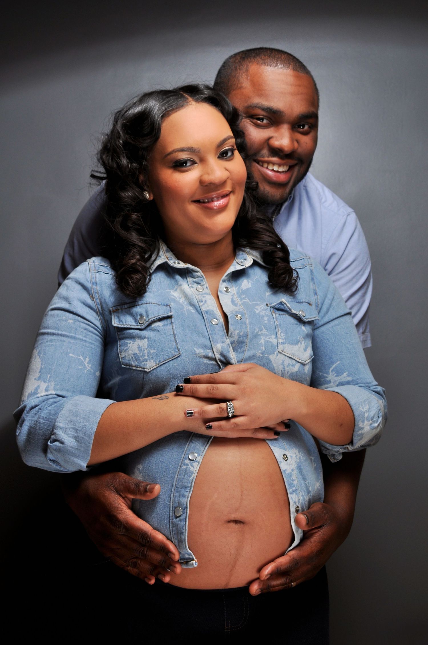 A happy couple poses for a maternity photo shoot, with the man embracing the pregnant woman from behind.
