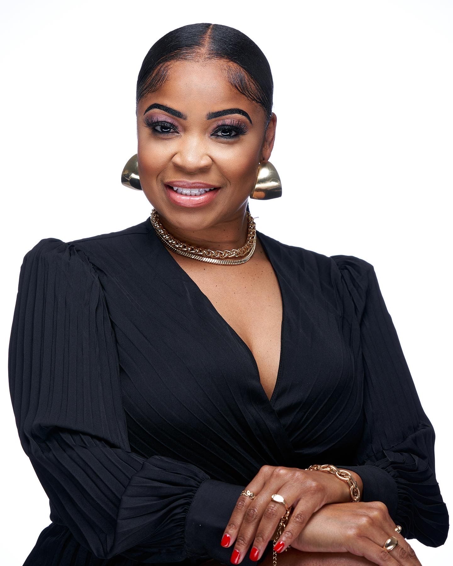 Woman in black blazer dress with gold jewelry smiling in professional portrait.