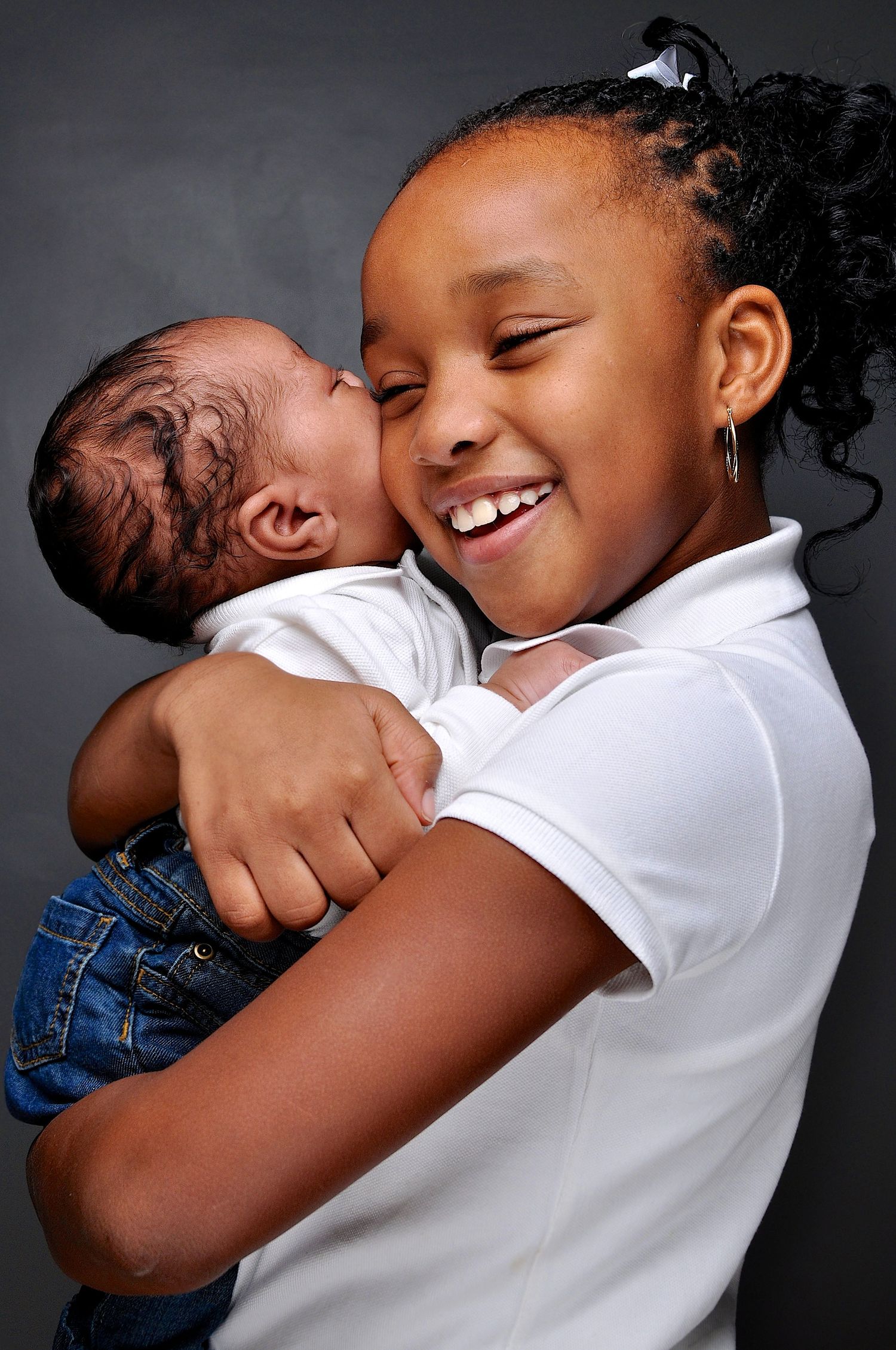 Smiling girl holding a newborn baby close, sharing a tender moment against a dark gray background.
