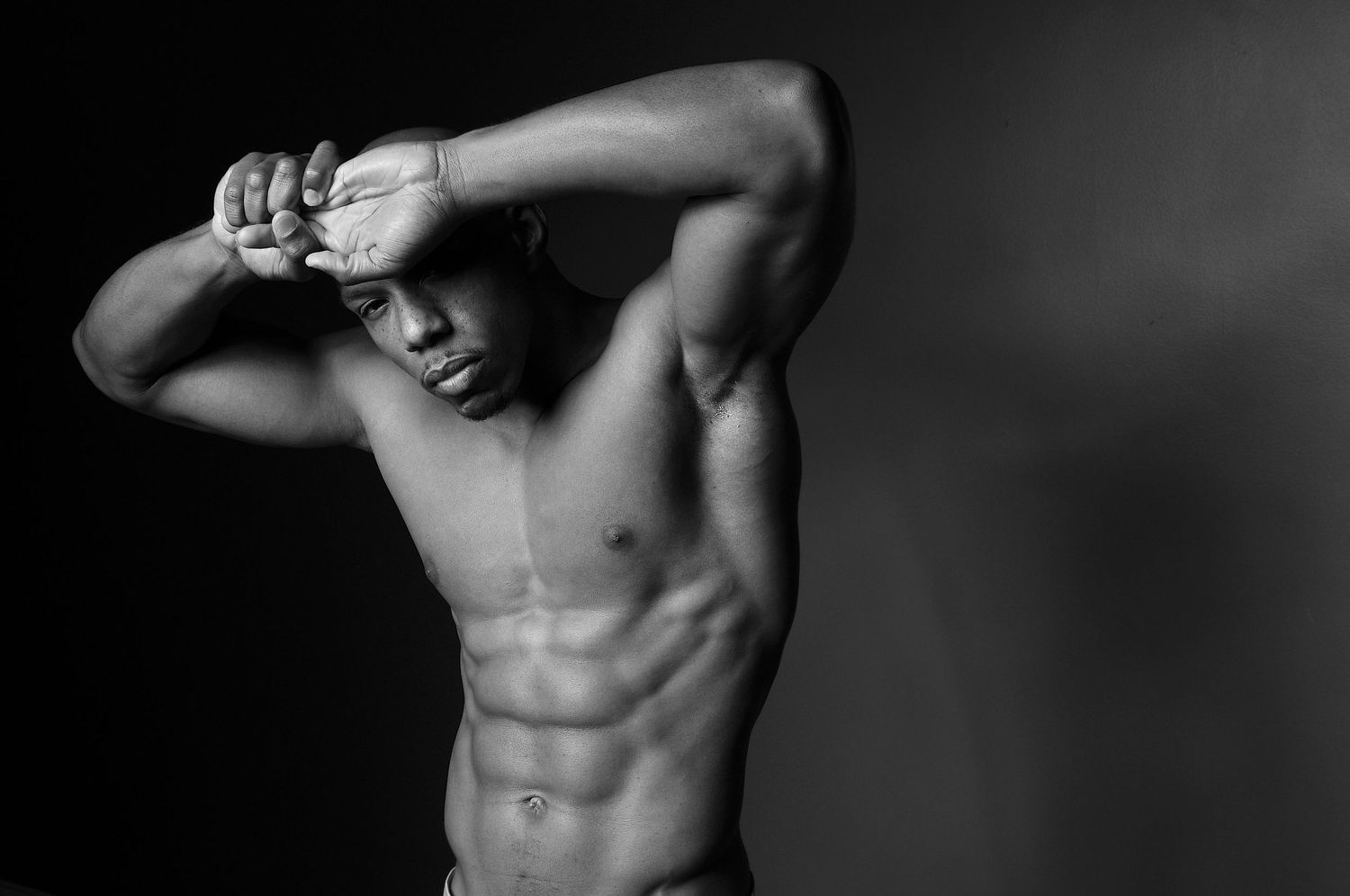 Black and white studio portrait of a muscular shirtless man posing with defined abs.