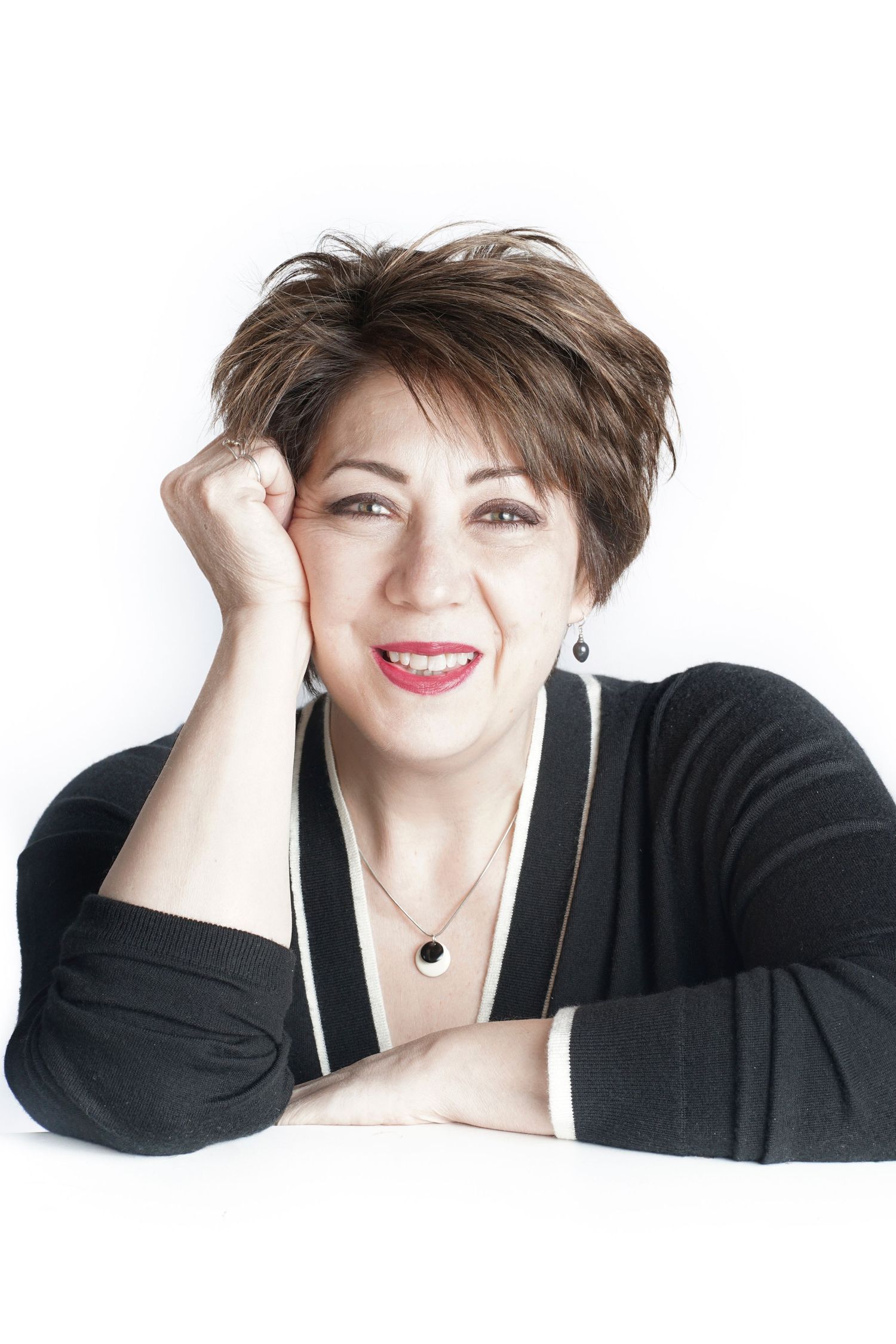 Middle-aged woman with short brown hair resting head on hand, smiling warmly.