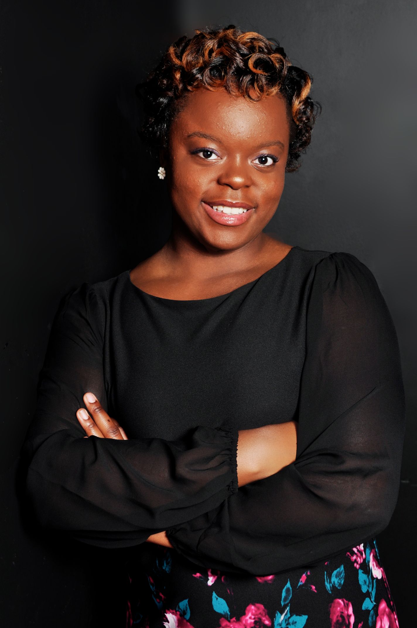 Confident Black woman in a black blouse with arms crossed smiling for a professional portrait.