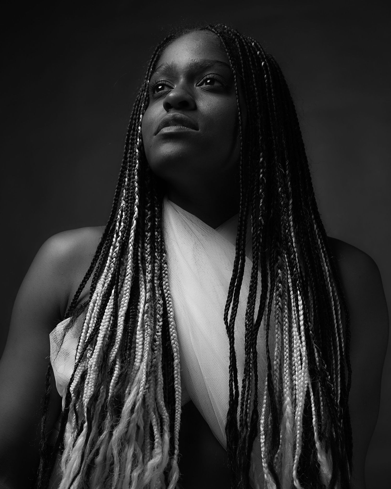 Dramatic black and white portrait of a Black woman with long box braids wearing a white draped top.