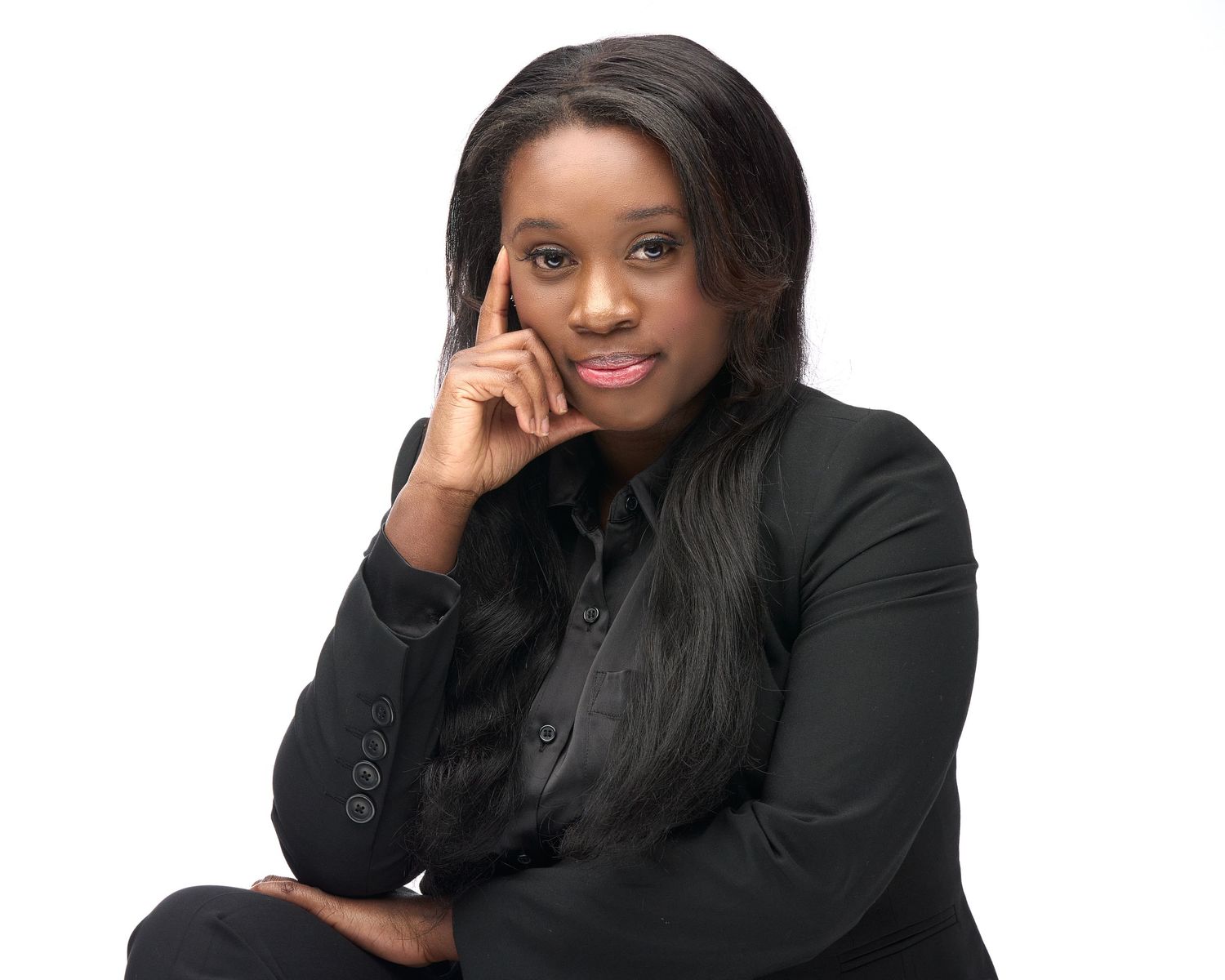 Professional Black woman in black blazer posing thoughtfully with hand raised to temple on white background.