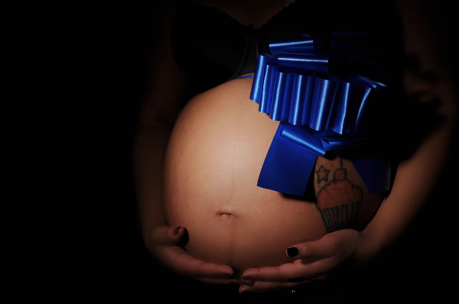 A pregnant belly adorned with a large blue bow, symbolizing a baby gift or gender reveal.