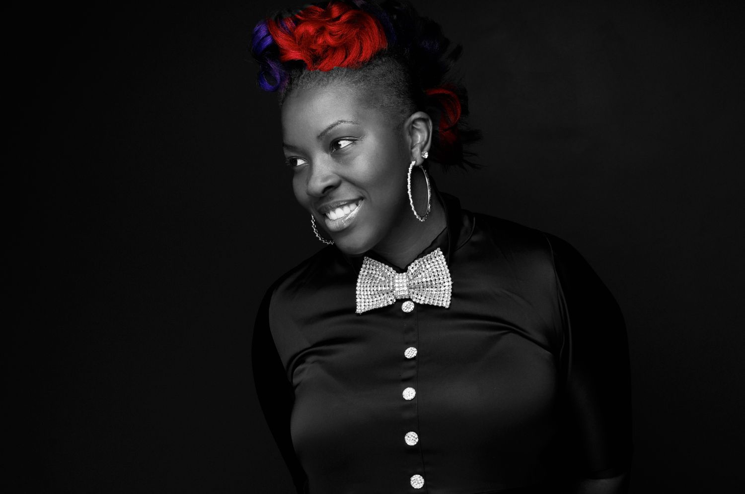 Stylish Black woman with colorful hair wearing a black button-up shirt with a rhinestone bow tie.
