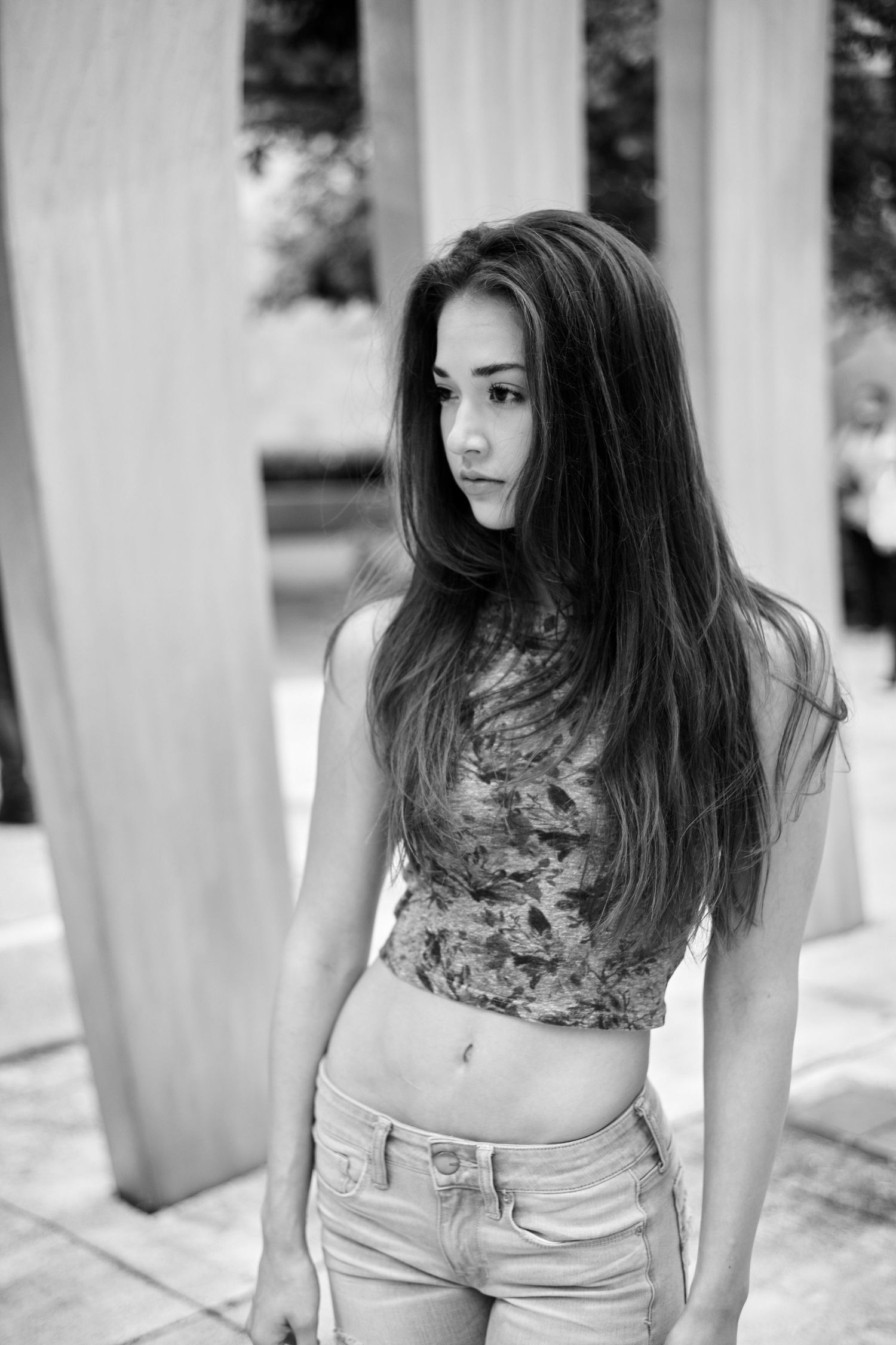 Young woman with long dark hair in crop top and jeans posing outdoors in black and white photo.