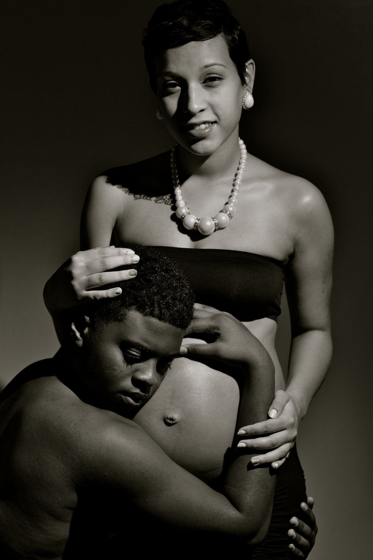 Black and white maternity portrait of a pregnant woman with partner embracing her baby bump.