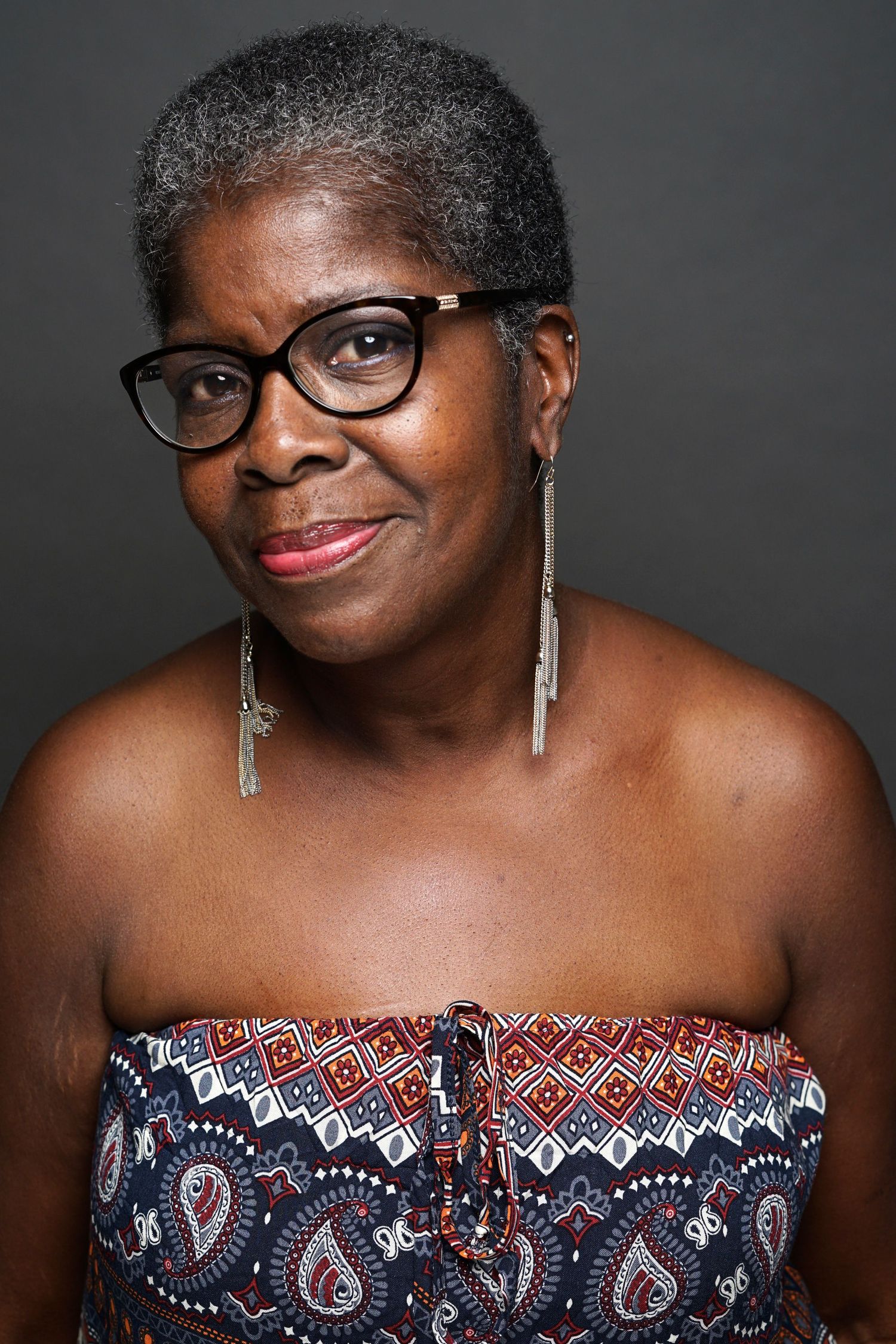 Older woman with gray hair, glasses, and colorful strapless top smiling warmly.