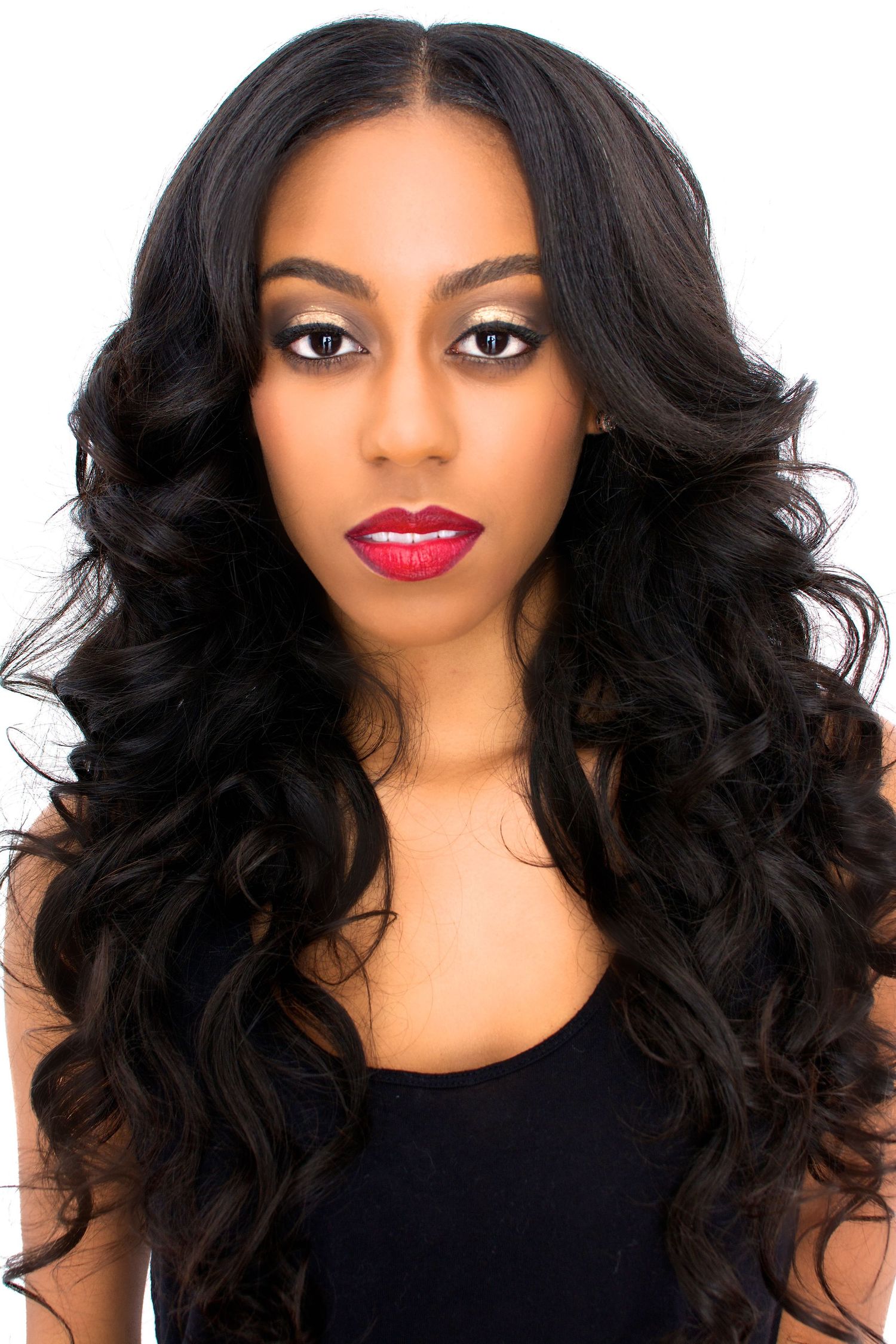 Woman with long wavy black hair and red lipstick posing against a white background.