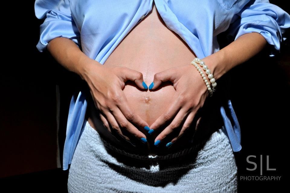 Close-up maternity photo of pregnant woman forming heart shape with hands over baby bump.