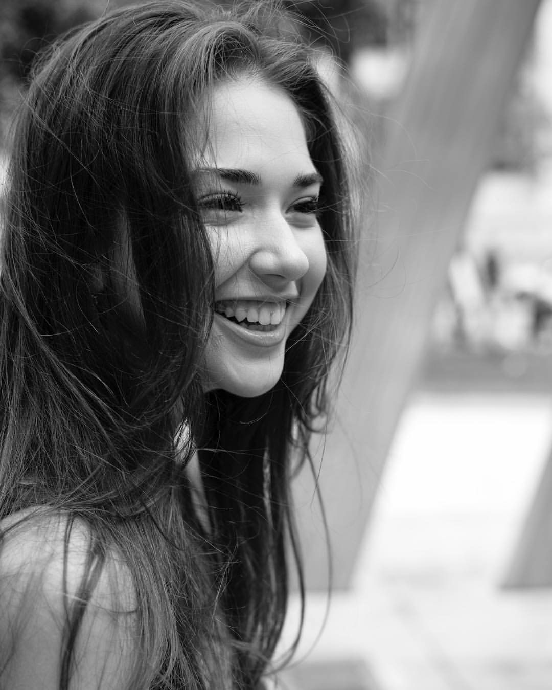 Candid black and white portrait of a smiling young woman with flowing hair outdoors.