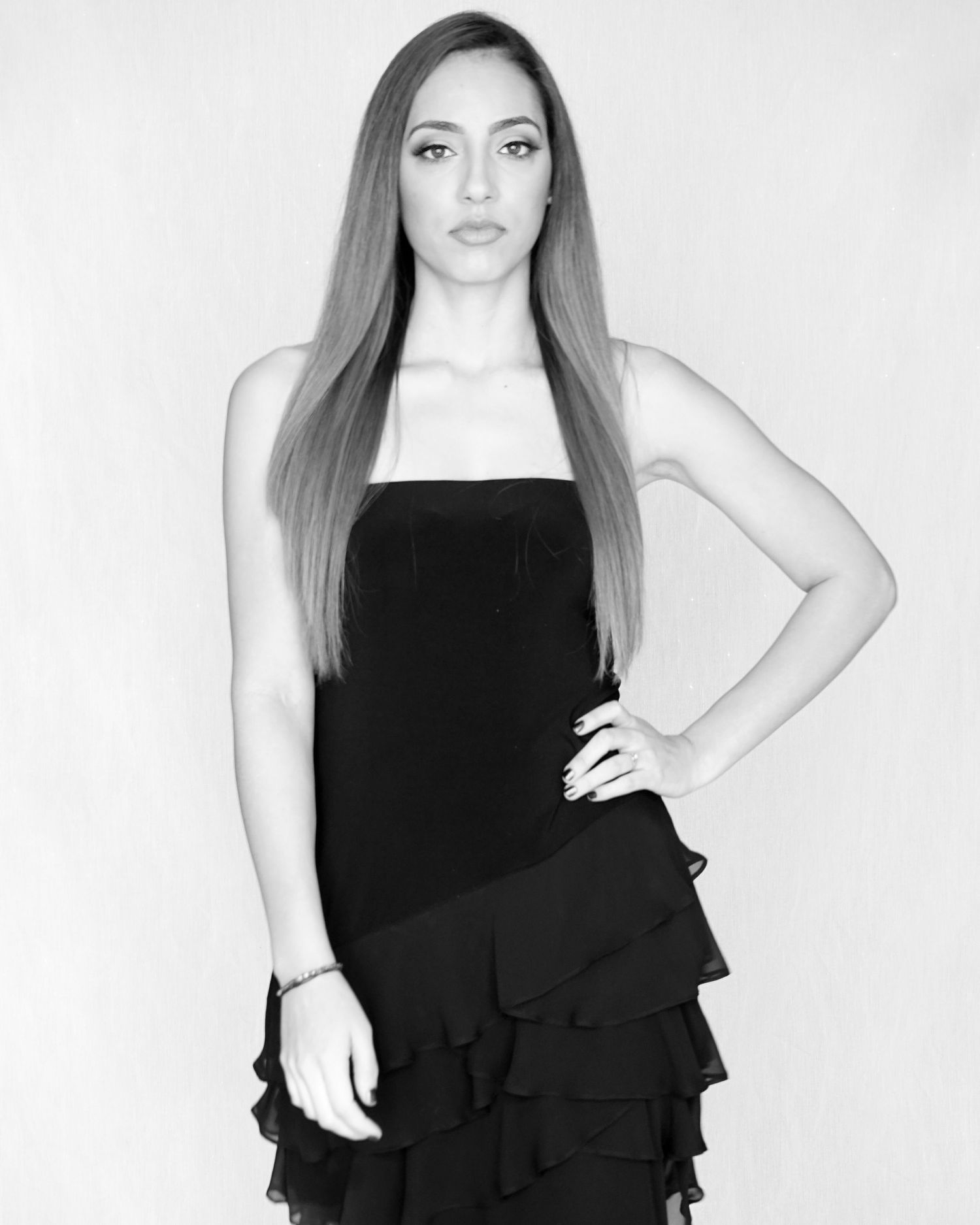 Black and white portrait of woman with long straight hair in strapless black ruffled dress.
