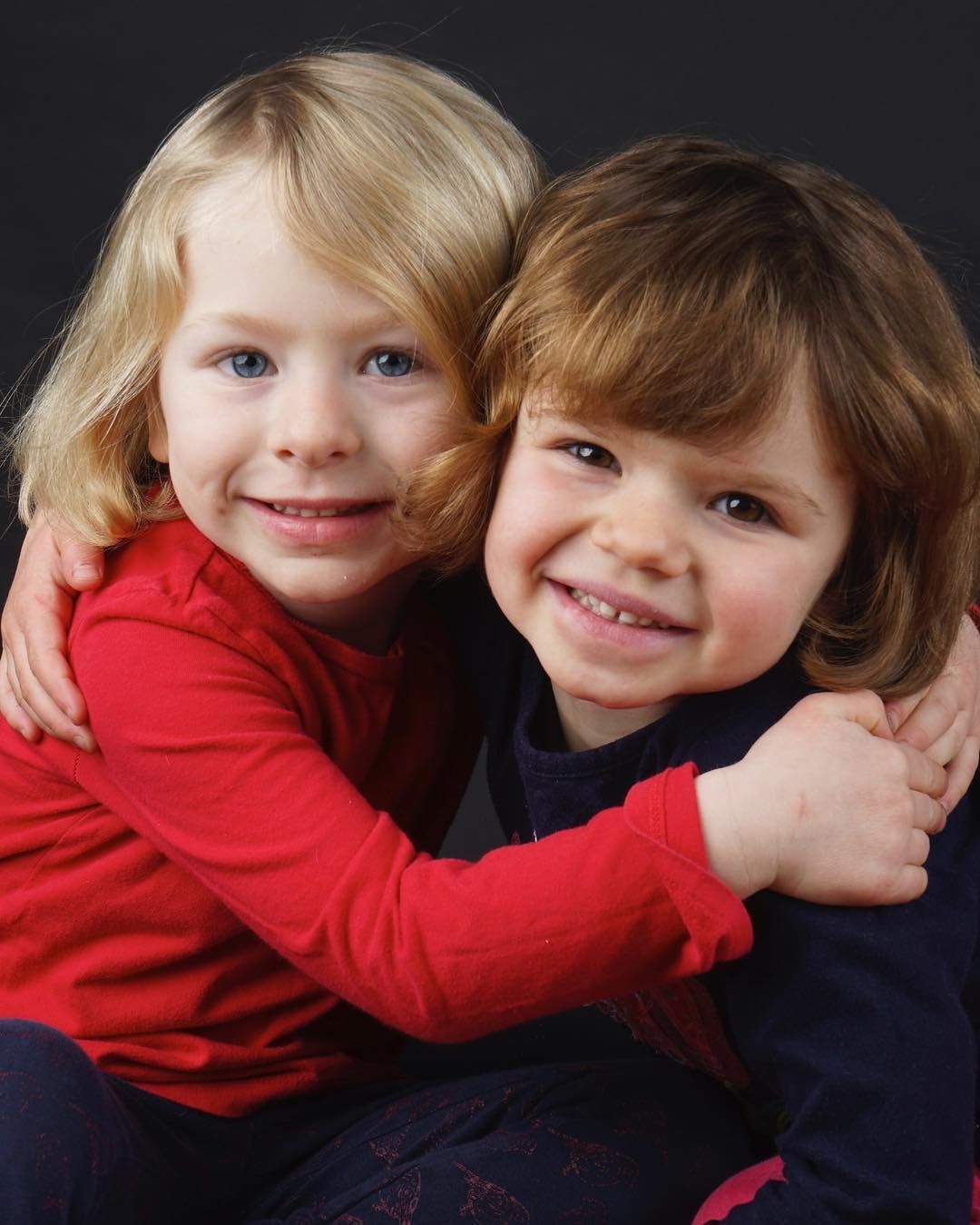 Two young children hugging and smiling, studio portrait on dark background.
