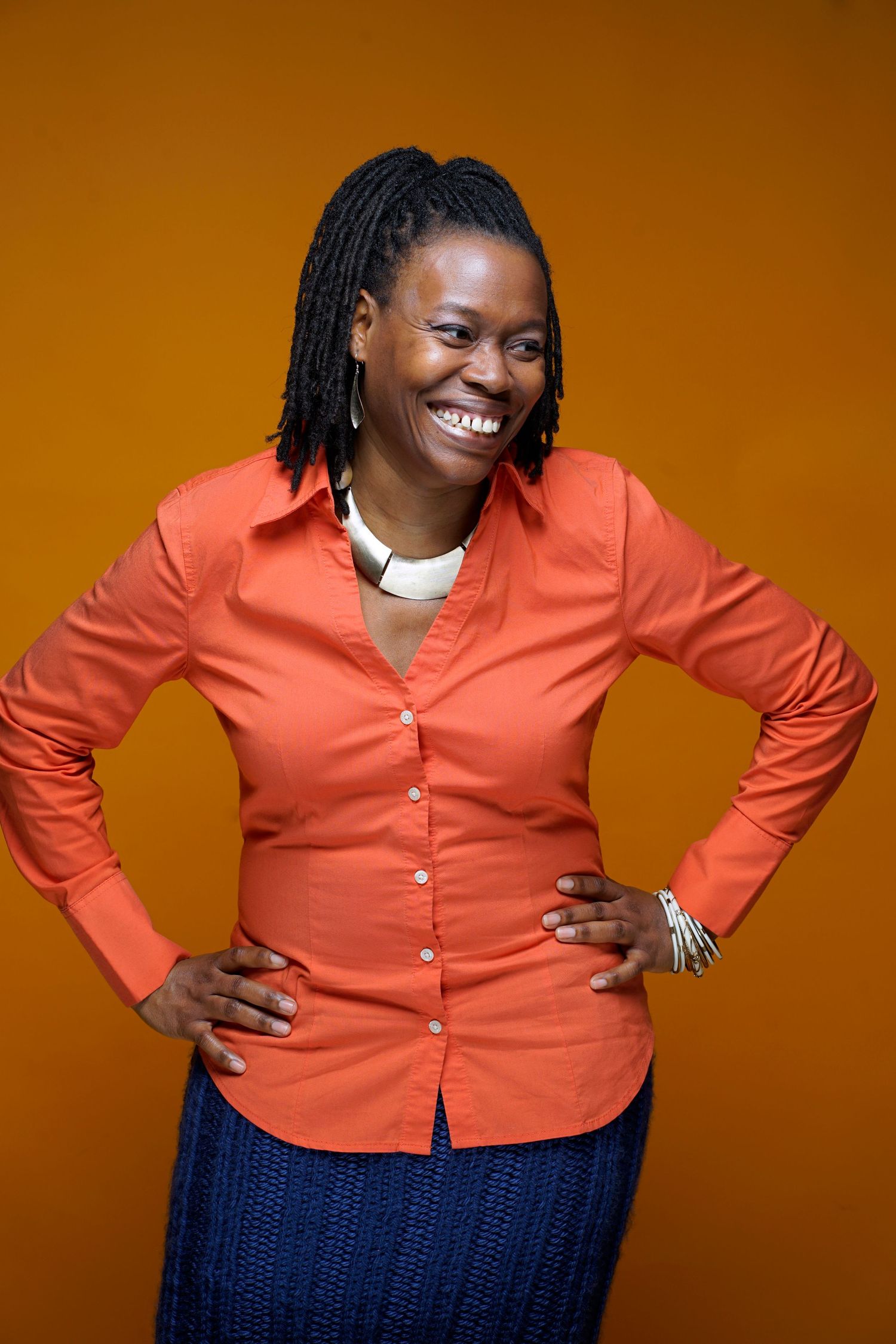 Woman in orange shirt with braids laughing joyfully against orange background.