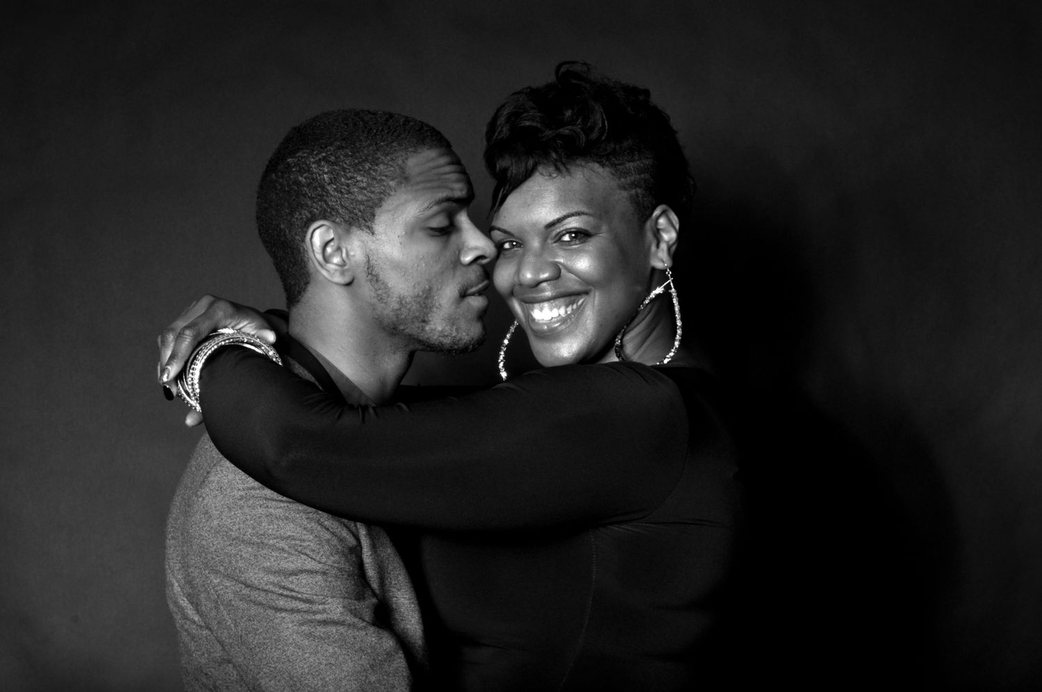 A joyful black-and-white portrait of a couple embracing, with the man kissing the woman on the cheek.