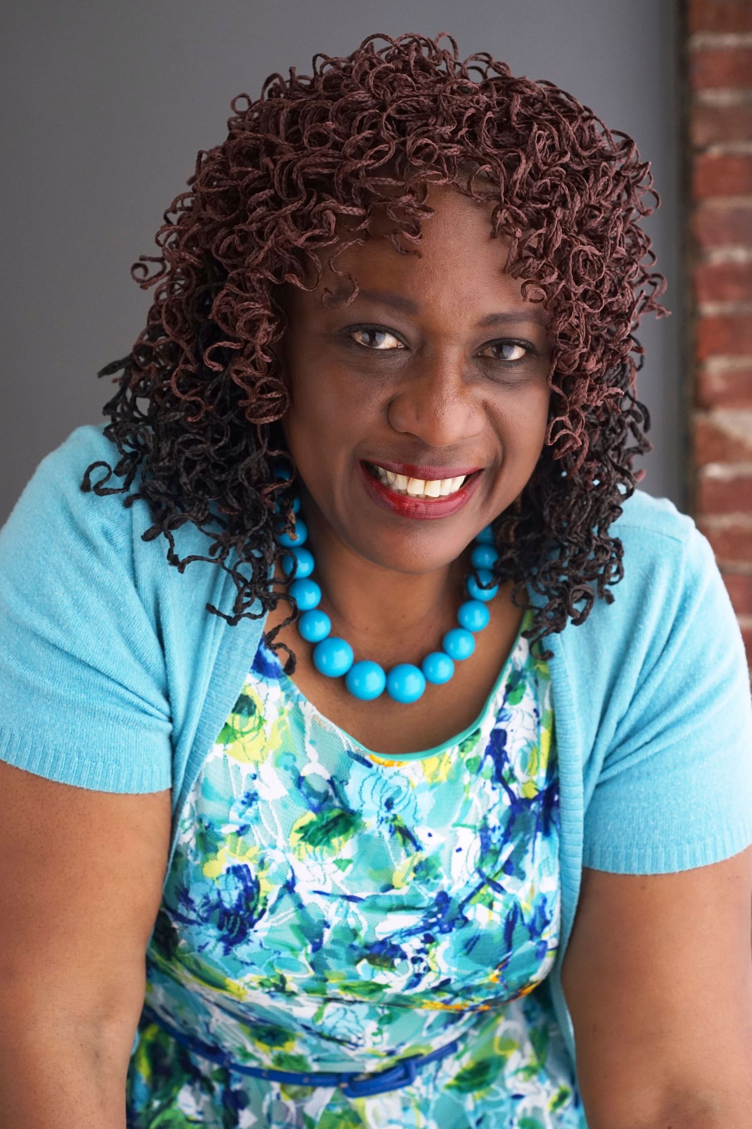 Smiling Black woman with curly hair wearing a turquoise necklace and floral dress.