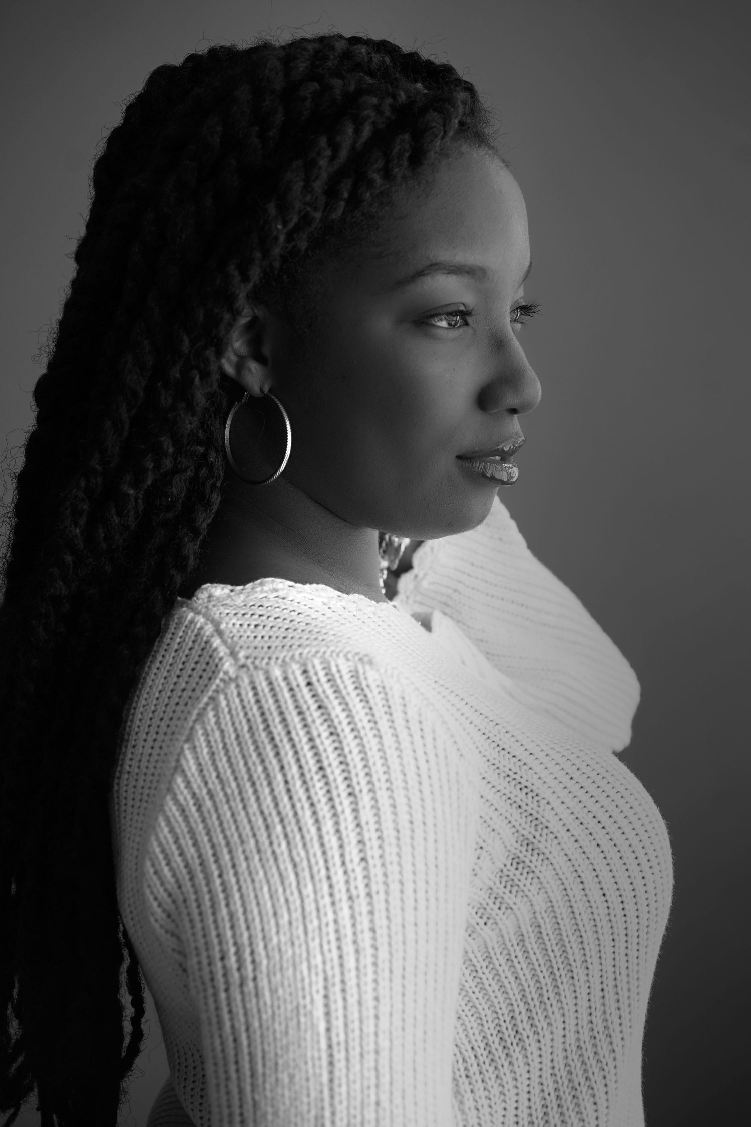 Black and white side profile portrait of a woman with long braids wearing a white knit sweater.
