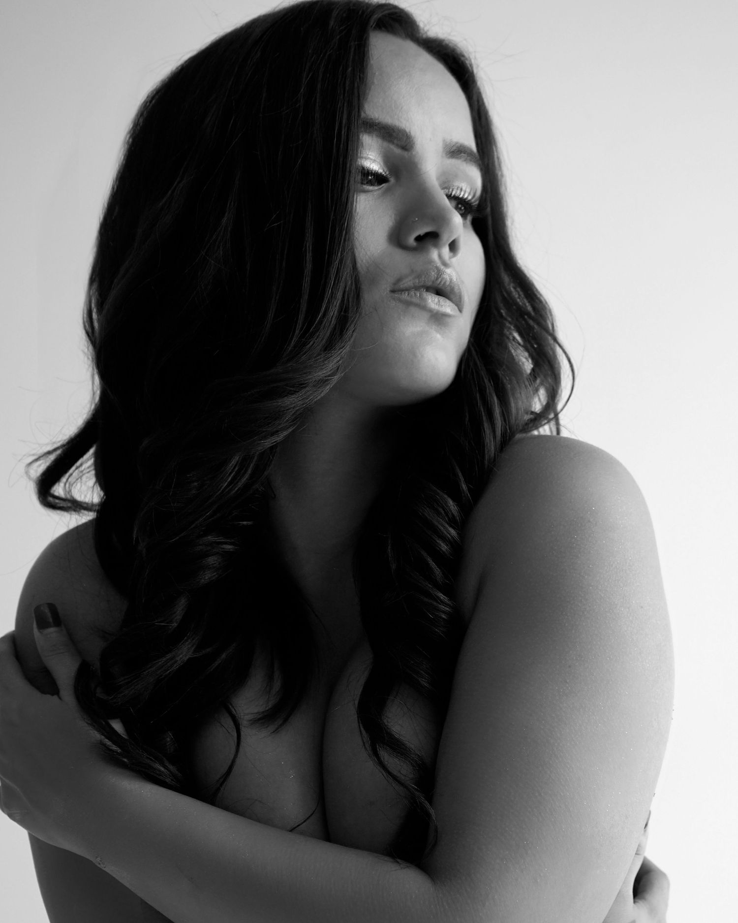 Black and white artistic portrait of a woman with dark curly hair crossing her arms over her chest.