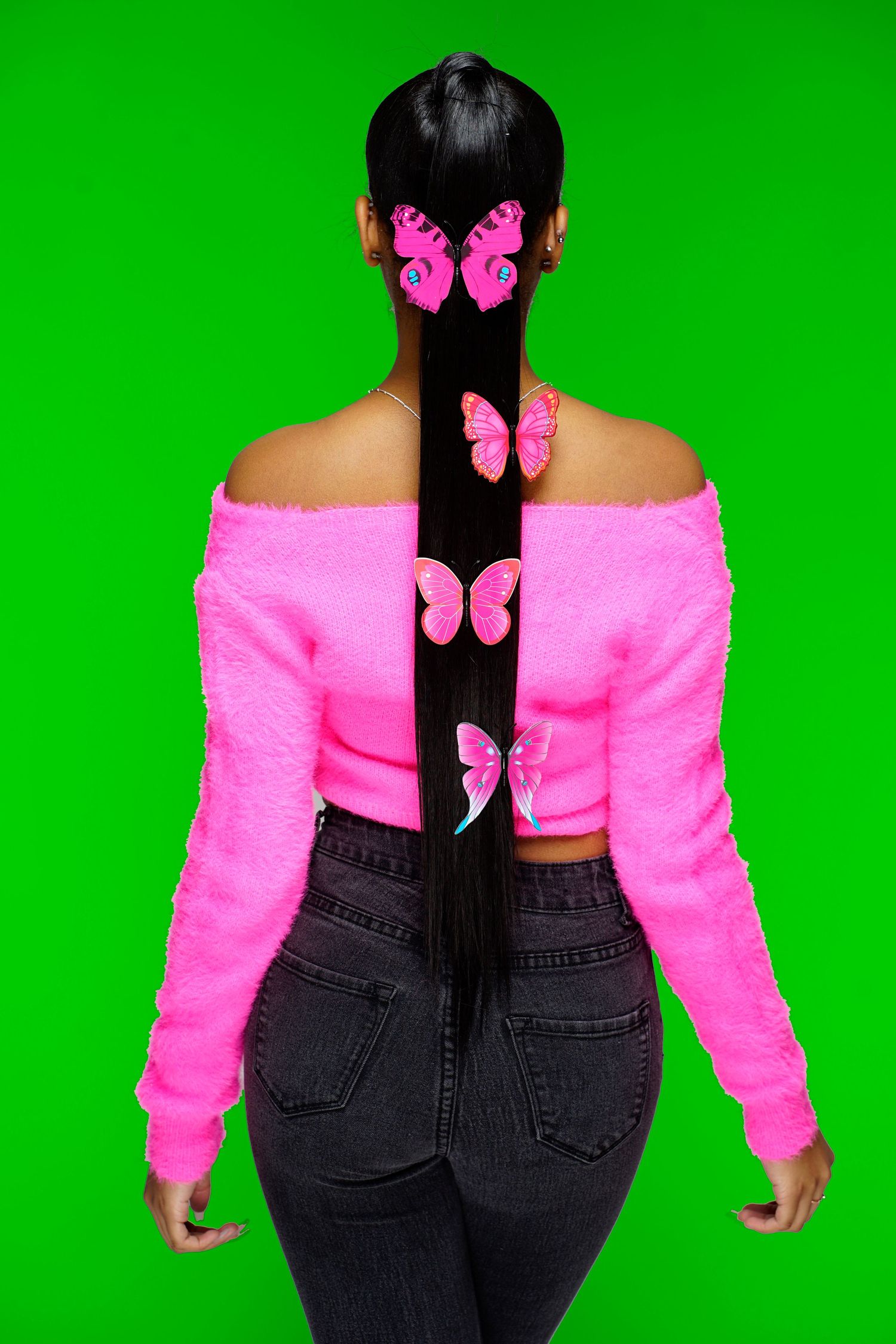 A woman seen from behind showcases a long dark ponytail with pink butterfly clips in a neon green studio.