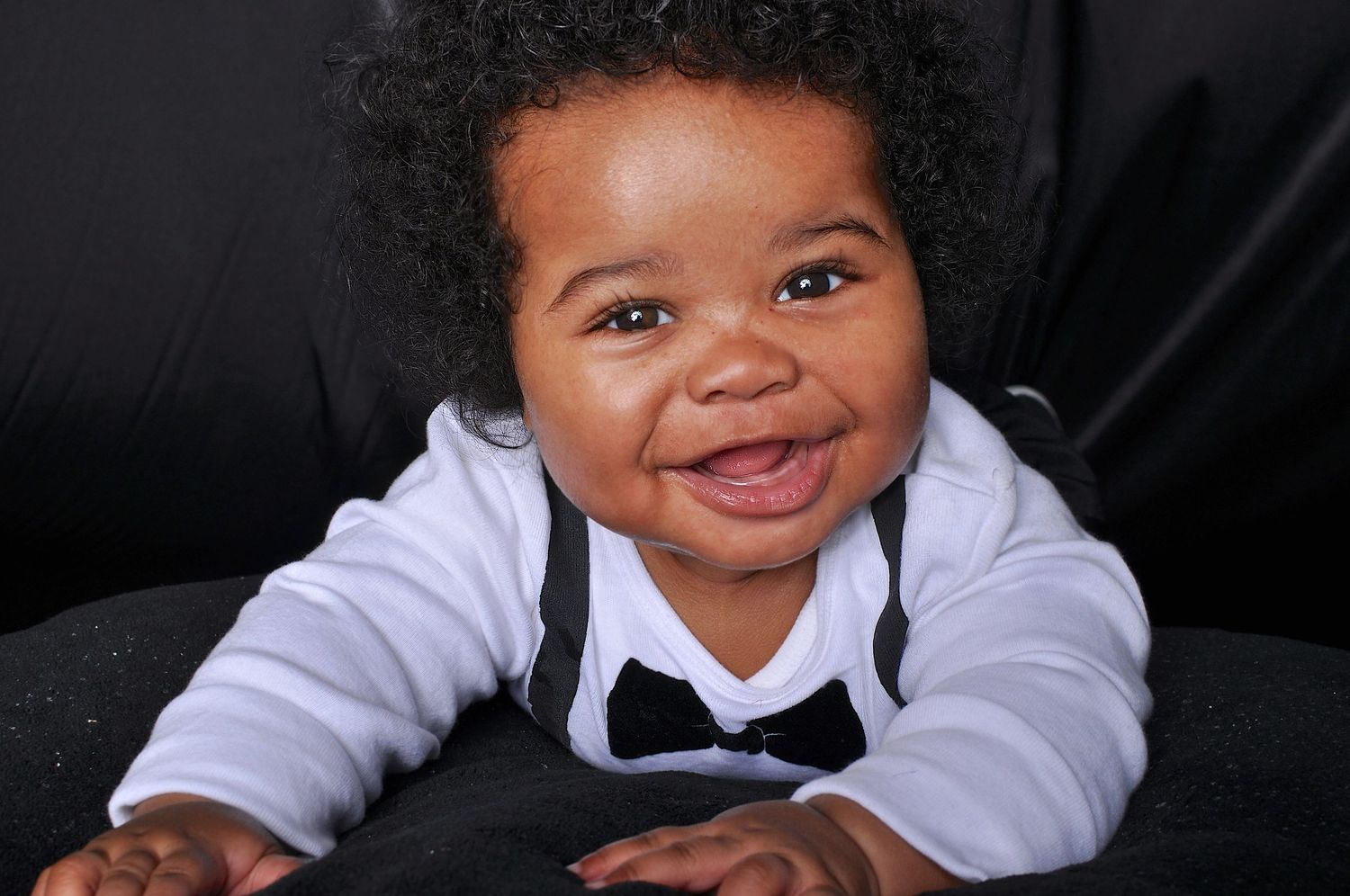 Happy Black baby boy in a white shirt with bow tie smiling brightly during a photo session.