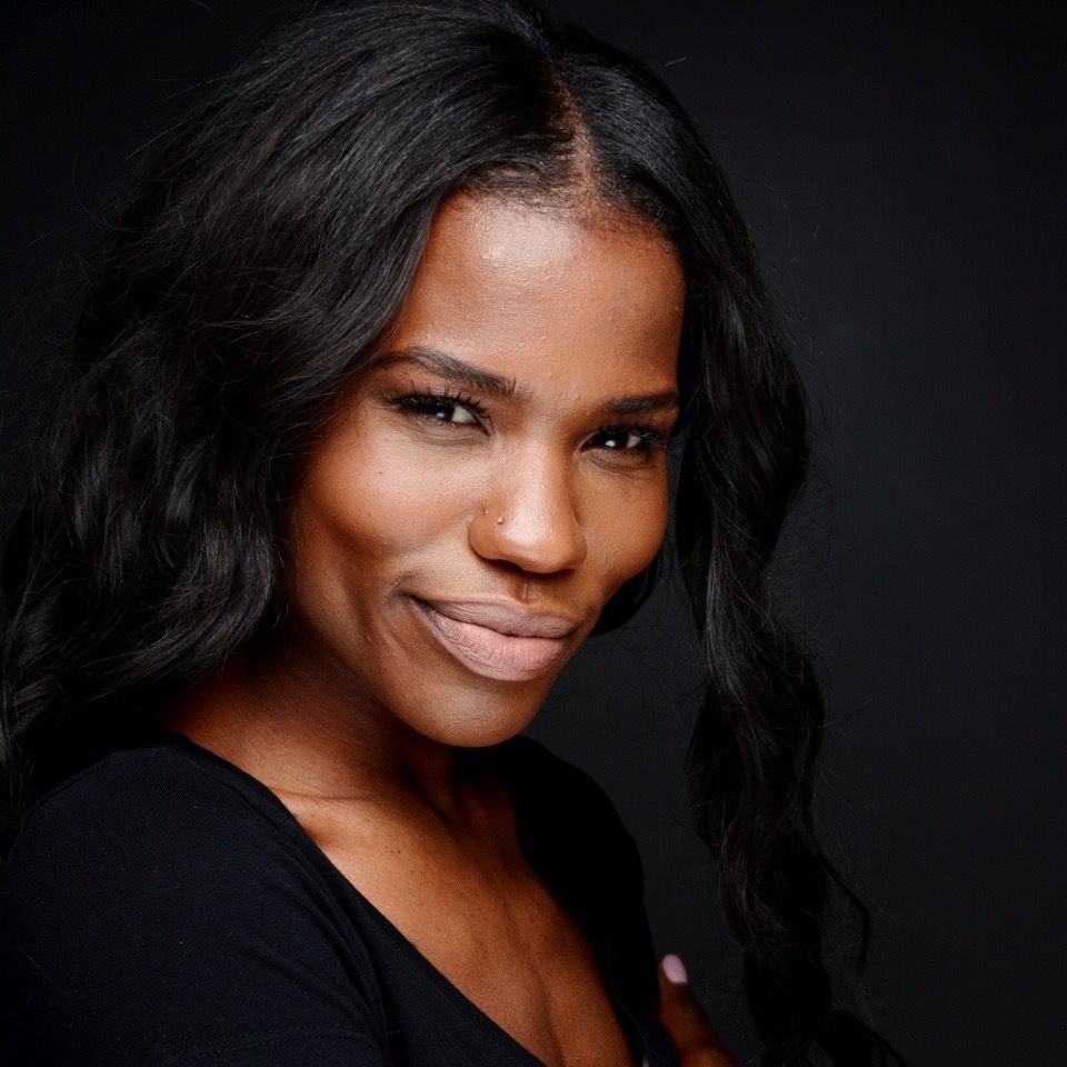 Professional headshot of a smiling Black woman with wavy hair wearing a black top against a dark background.