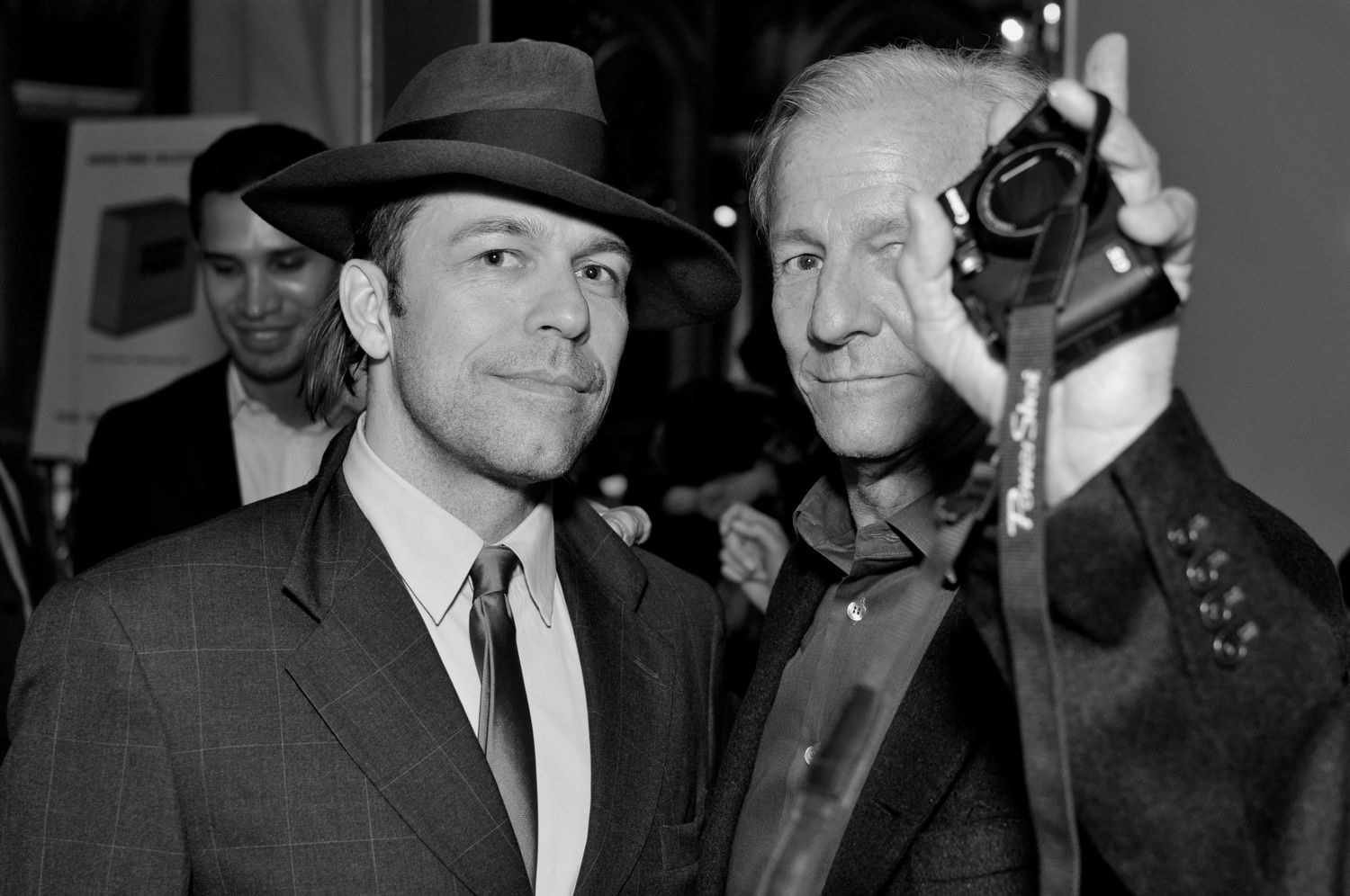 Two men posing together in black and white photo, one holding a camera at an event.