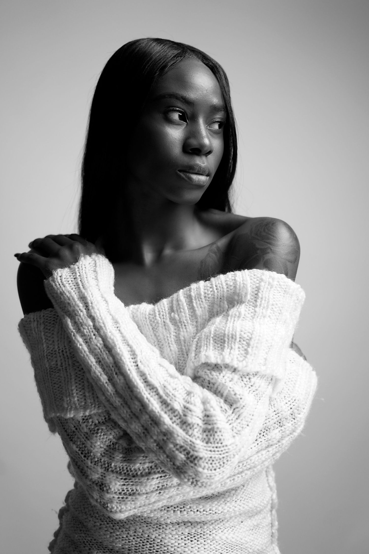 Black and white portrait of a woman in an off-shoulder white knit sweater with a serene expression.