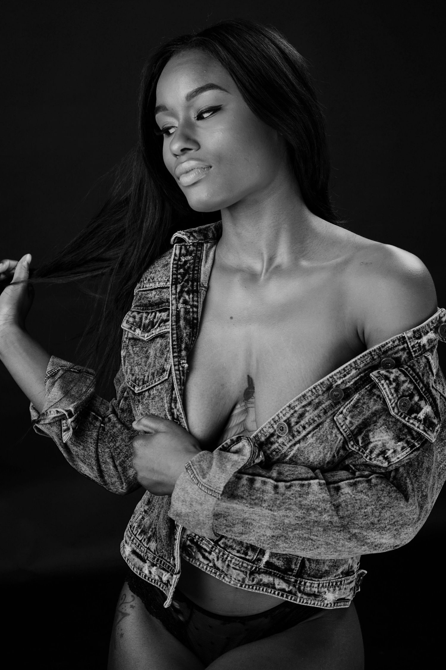 A young woman poses dramatically in a denim jacket in a black and white studio portrait.