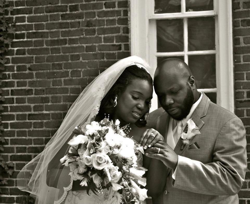 Black and white photo of a bride and groom sharing an intimate moment outside a brick building.