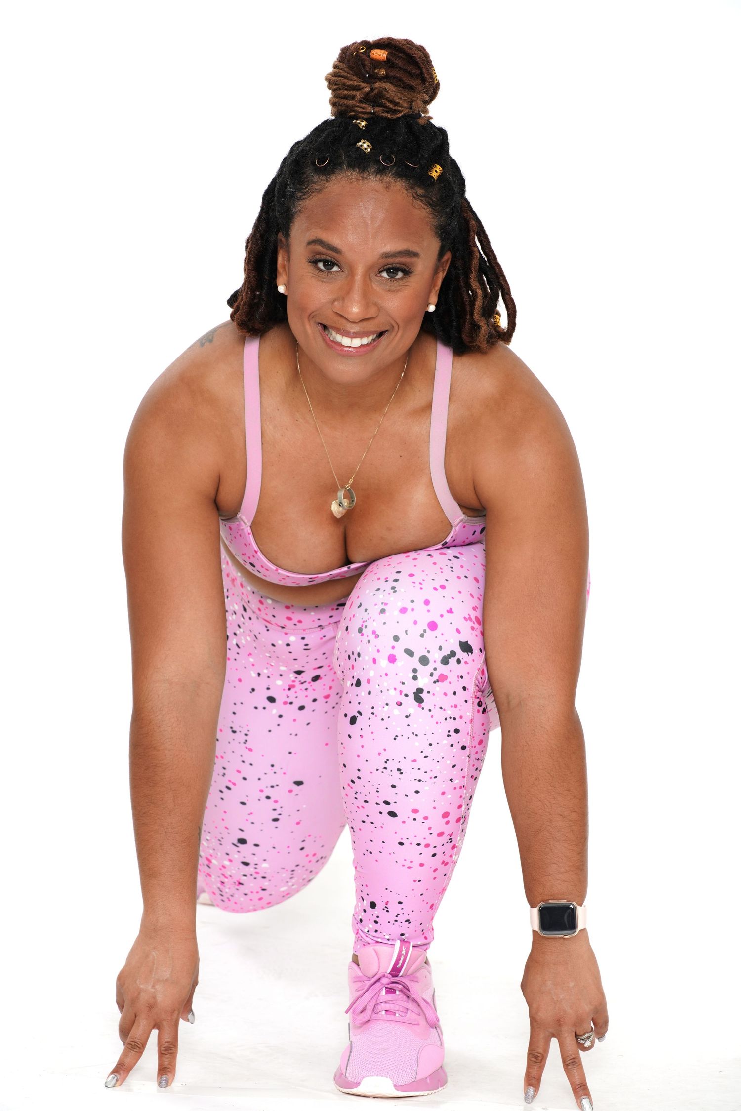 Smiling woman in pink workout set in athletic starting position pose against white background.
