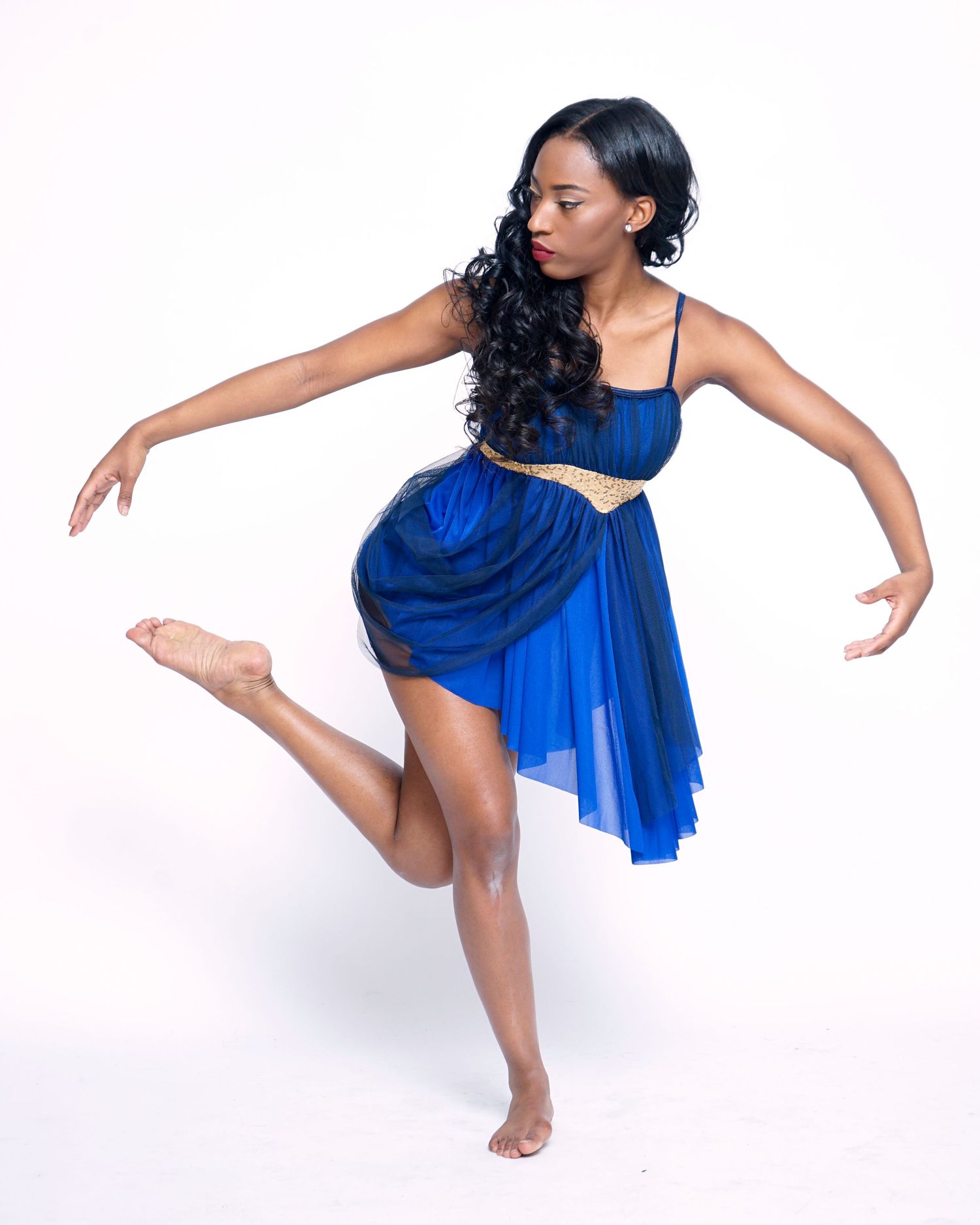Young Black female dancer in blue dress performing a graceful ballet pose on white background.