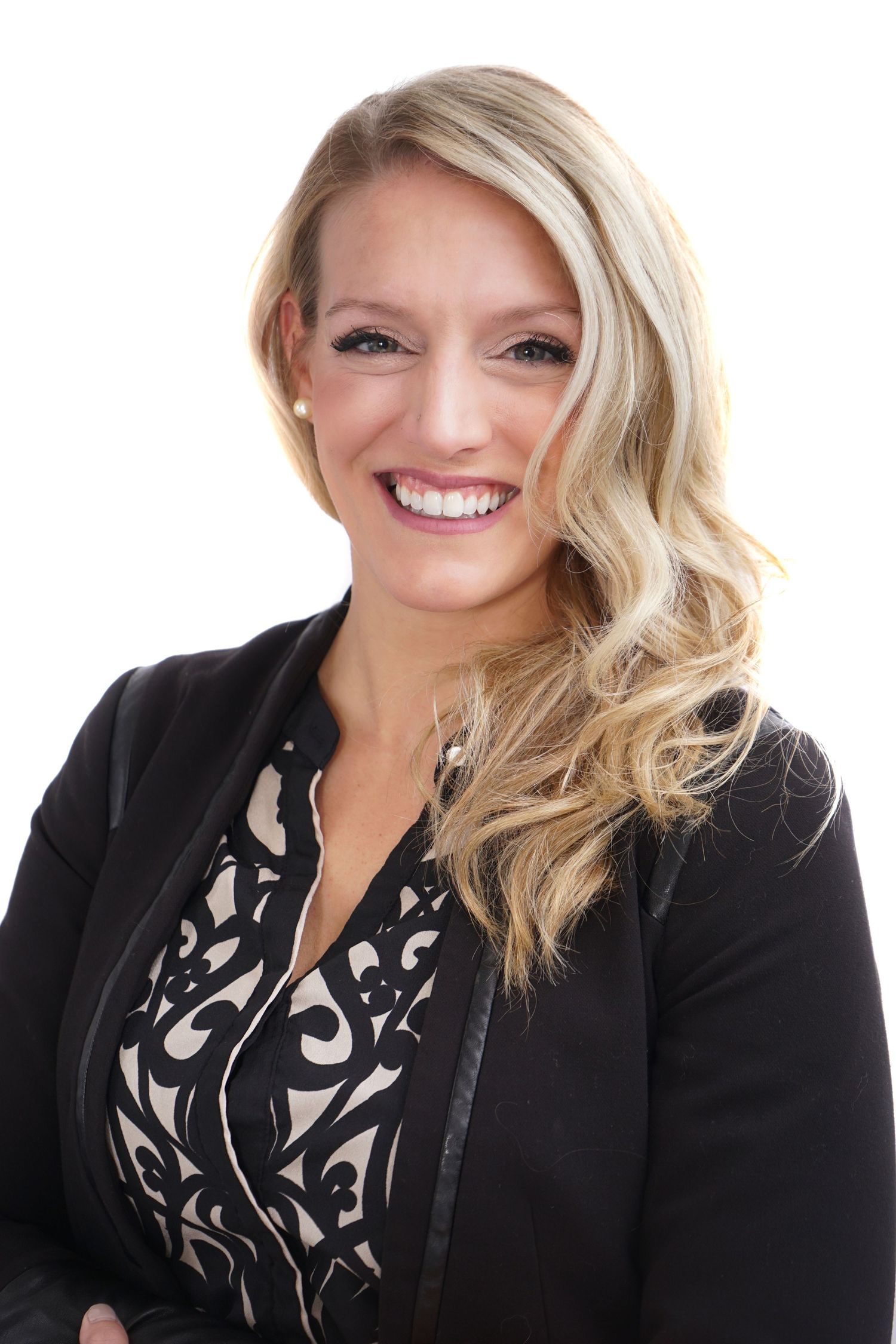 Blonde woman in black blazer smiling confidently, professional business headshot on white background.