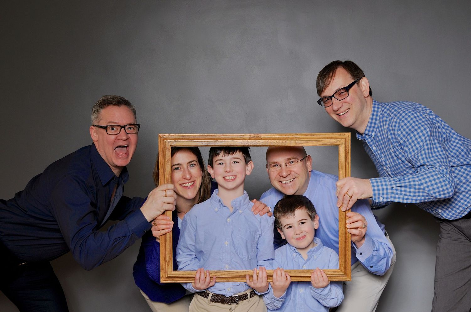 Happy family of five posing playfully with a decorative gold picture frame in a studio portrait.