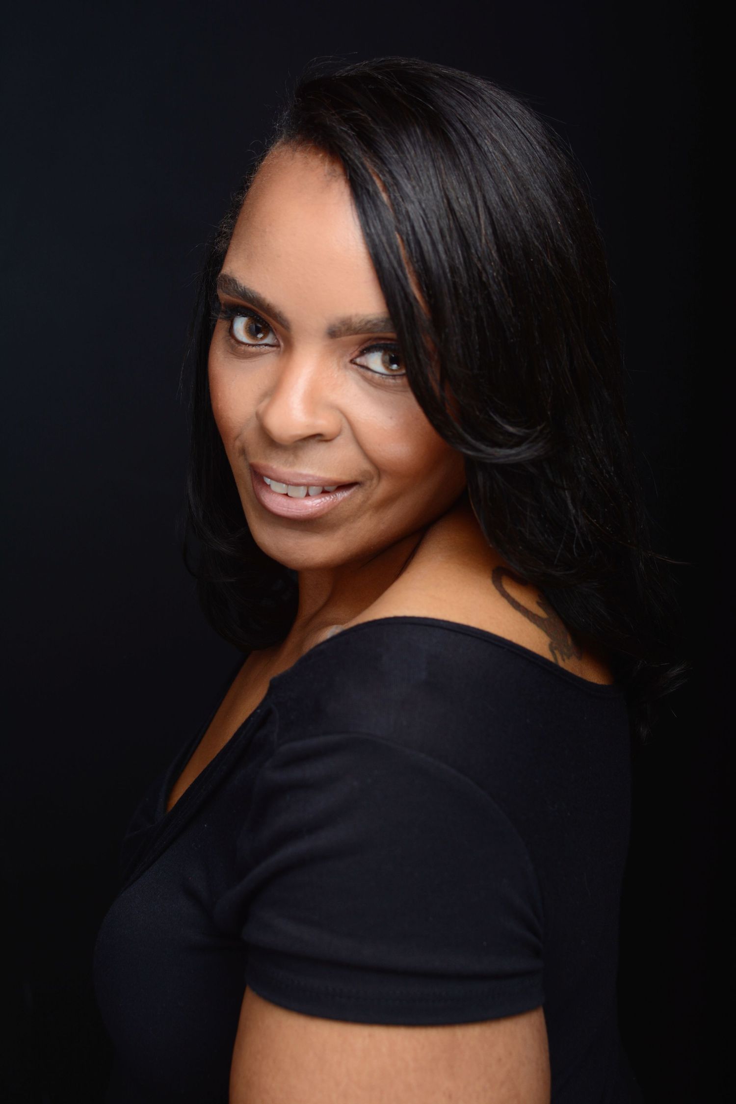 Elegant Black woman in black top with long dark hair against dark background.