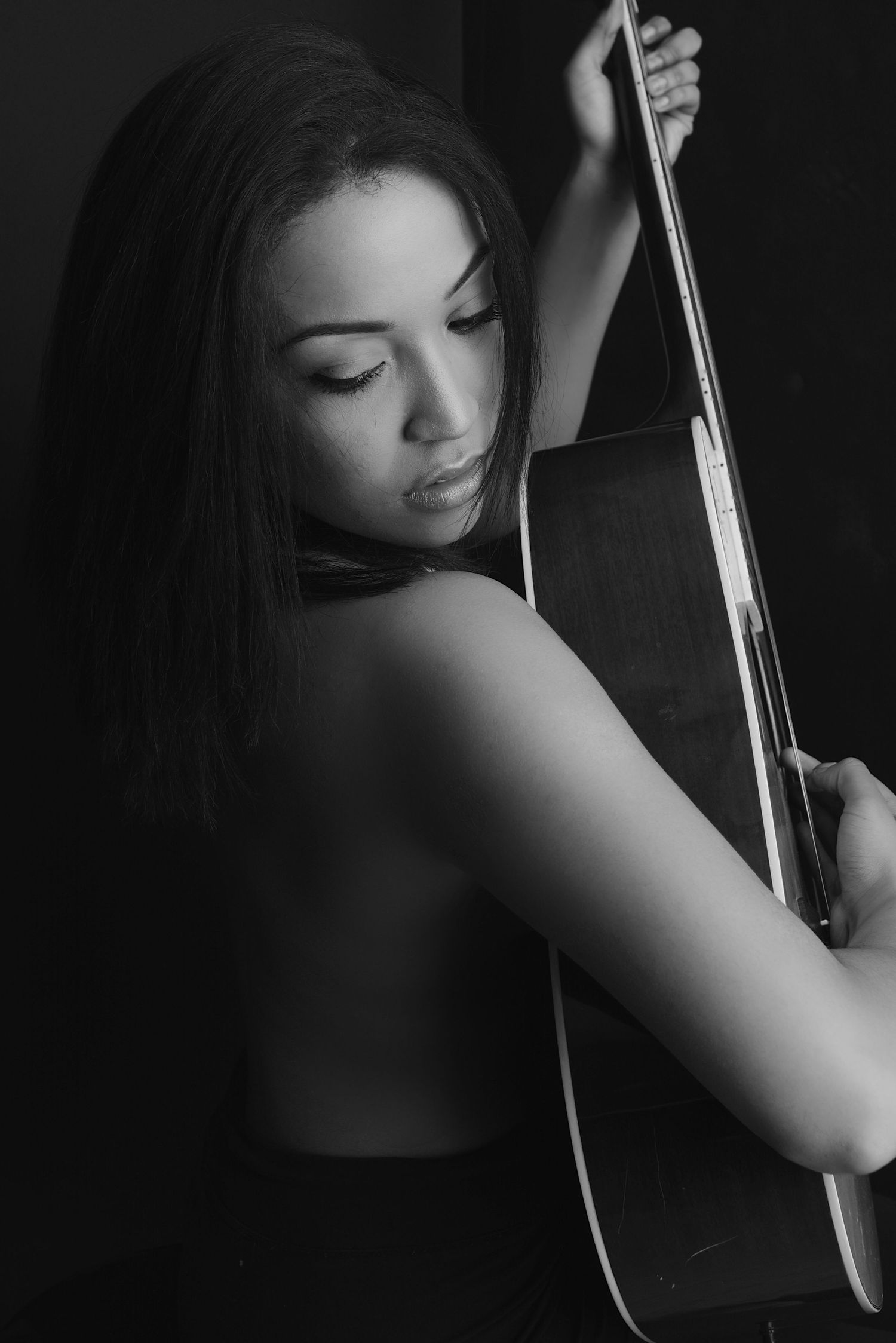 Black and white portrait of a young woman holding an acoustic guitar against a dark background.