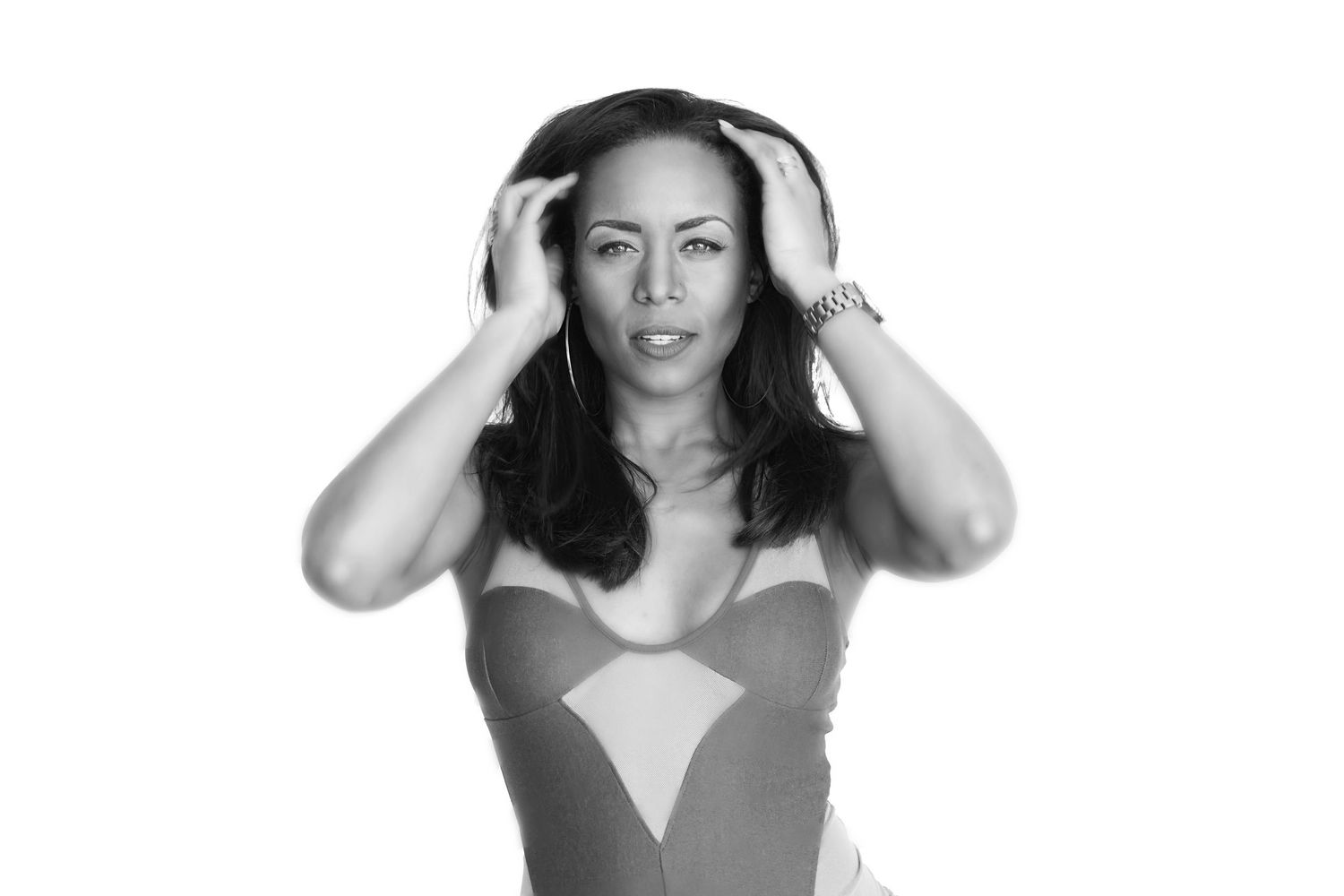 Black and white photo of woman in geometric swimsuit holding her head with both hands.