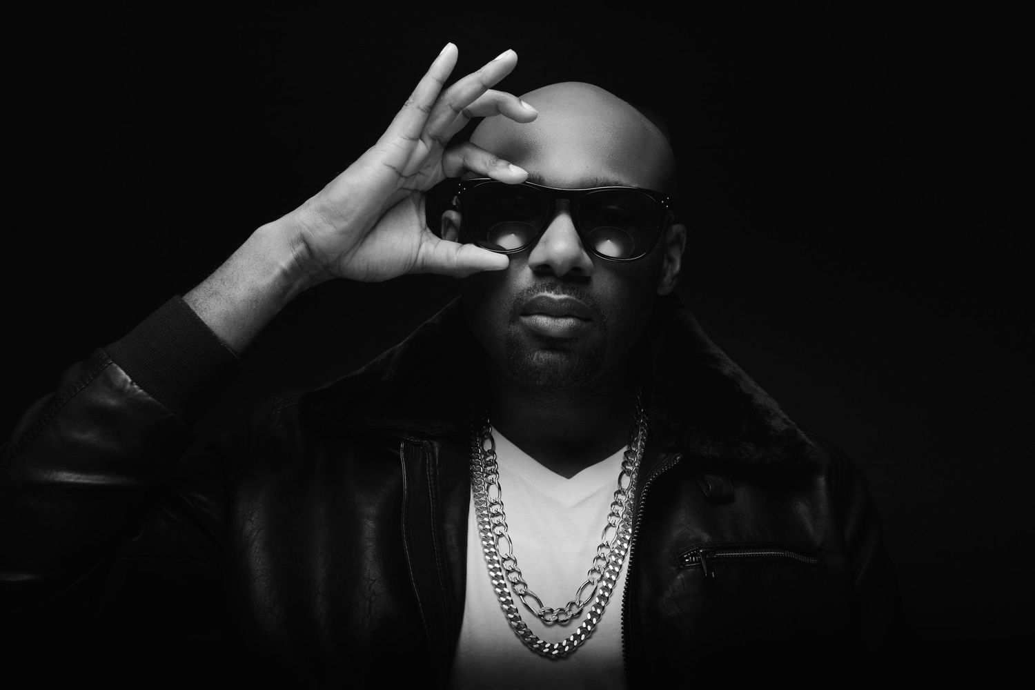 Stylish Black man wearing sunglasses and a chain necklace posing in a black and white photo.