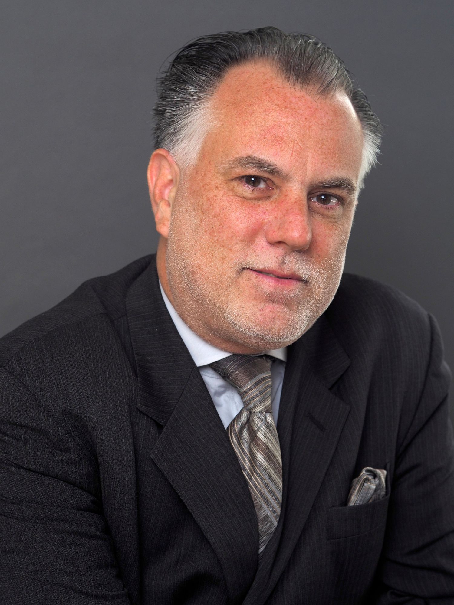 A distinguished older man with gray hair in a dark suit and tie poses for a professional headshot.