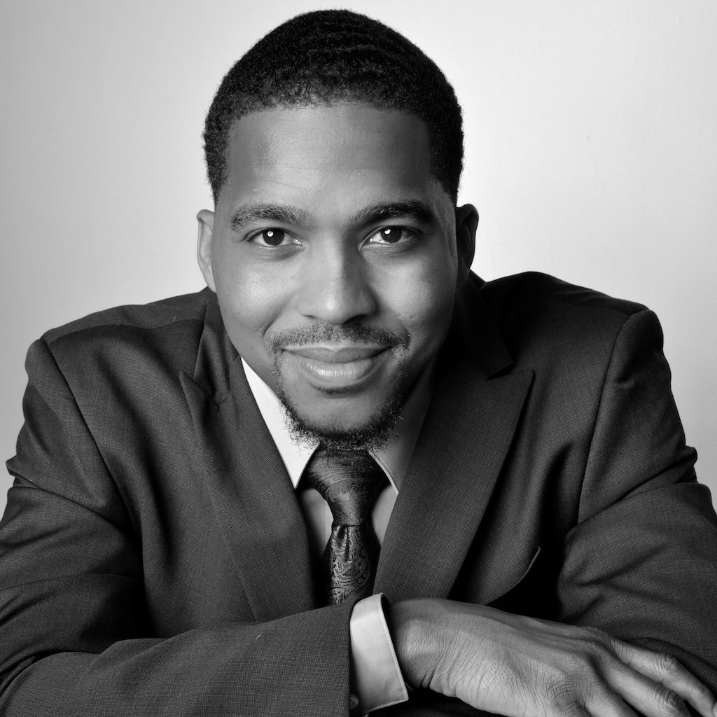 Professional black and white portrait of a man in a suit and tie, smiling confidently.