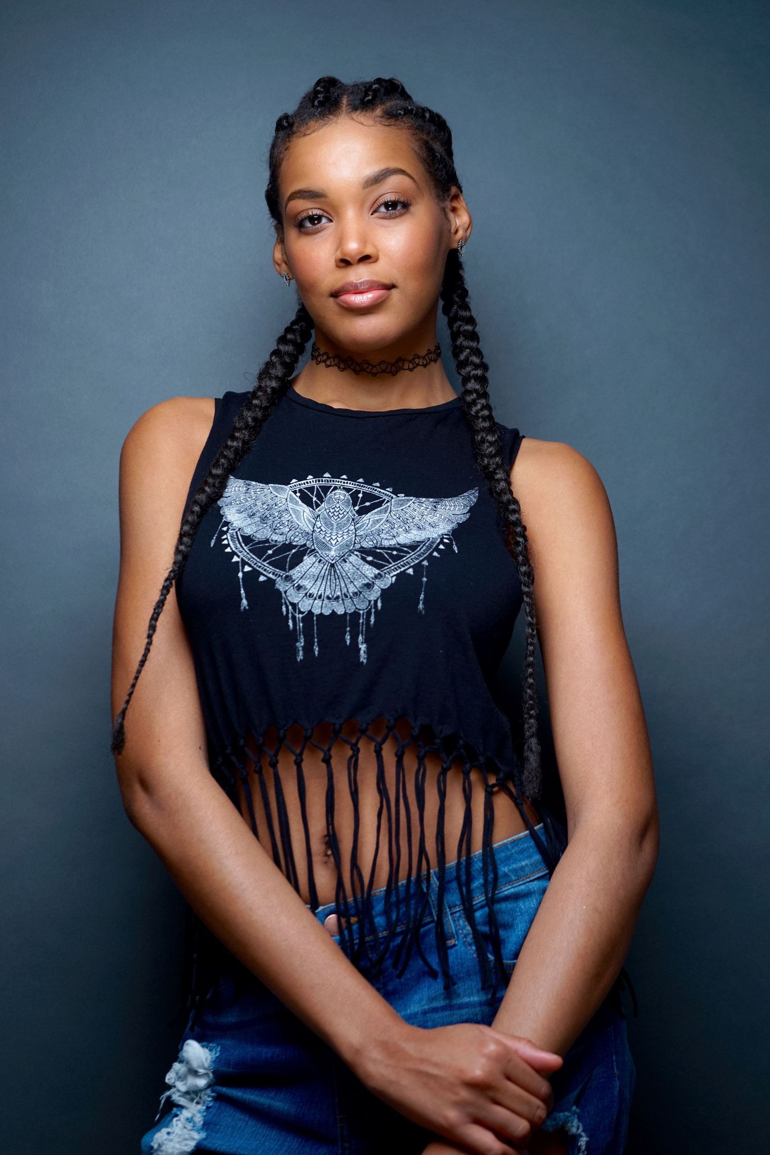 Young woman with box braids wearing a black fringe crop top with eagle graphic and ripped jeans.